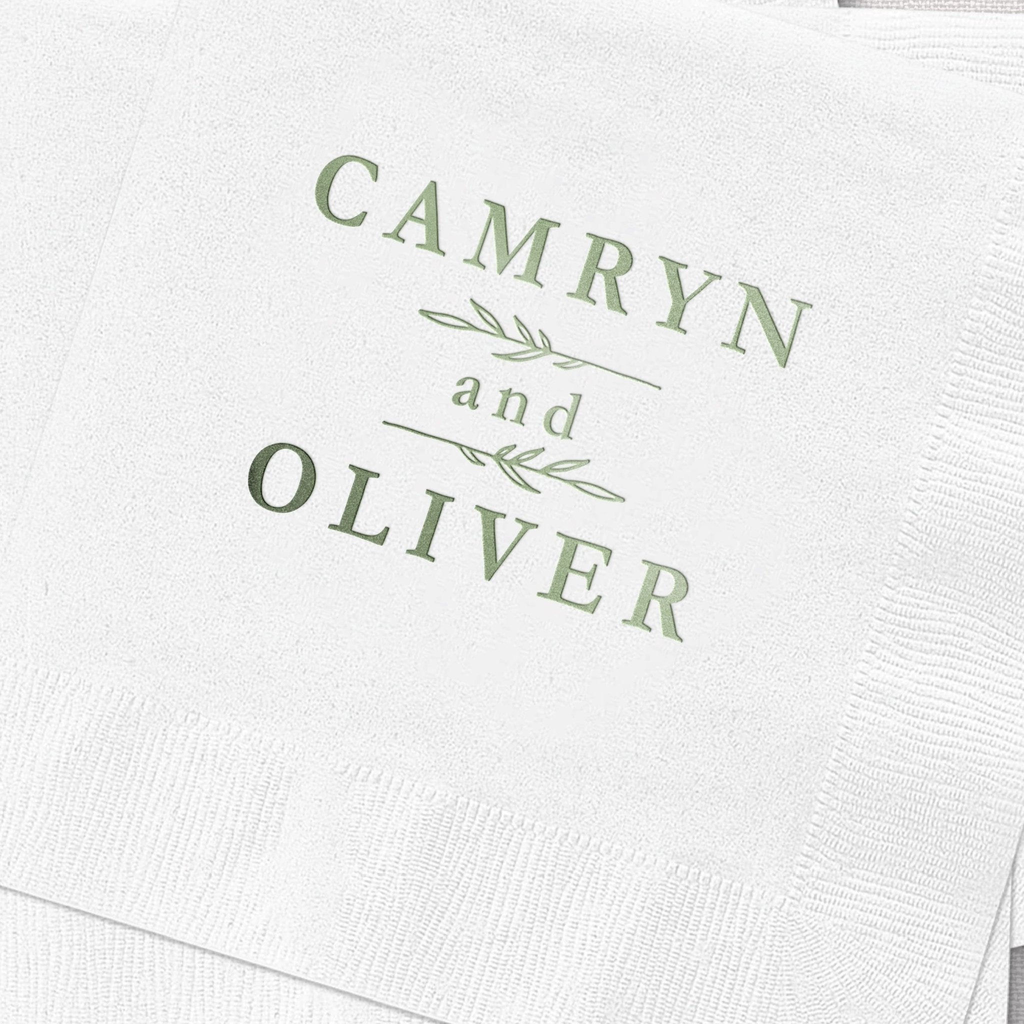 White napkin with sage green foil-stamped names "Camryn and Oliver" with botanical leaf design between names