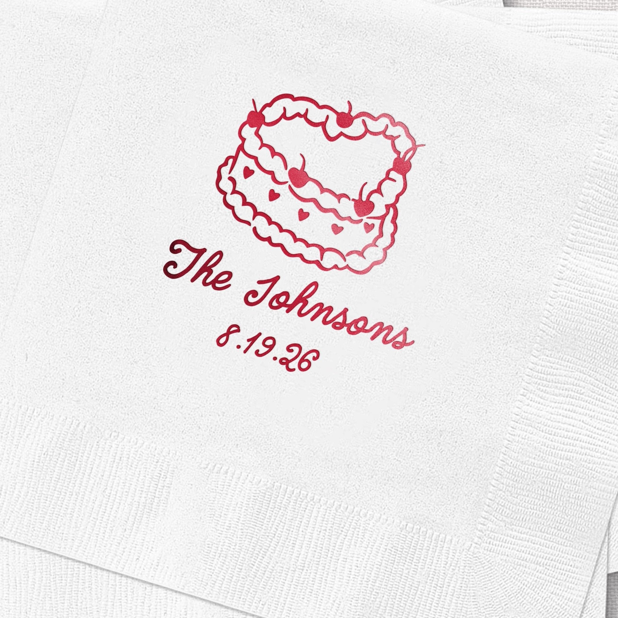 White cocktail napkin with red foil-stamped whimsical cake design and "The Johnsons 5.19.25" personalization text.