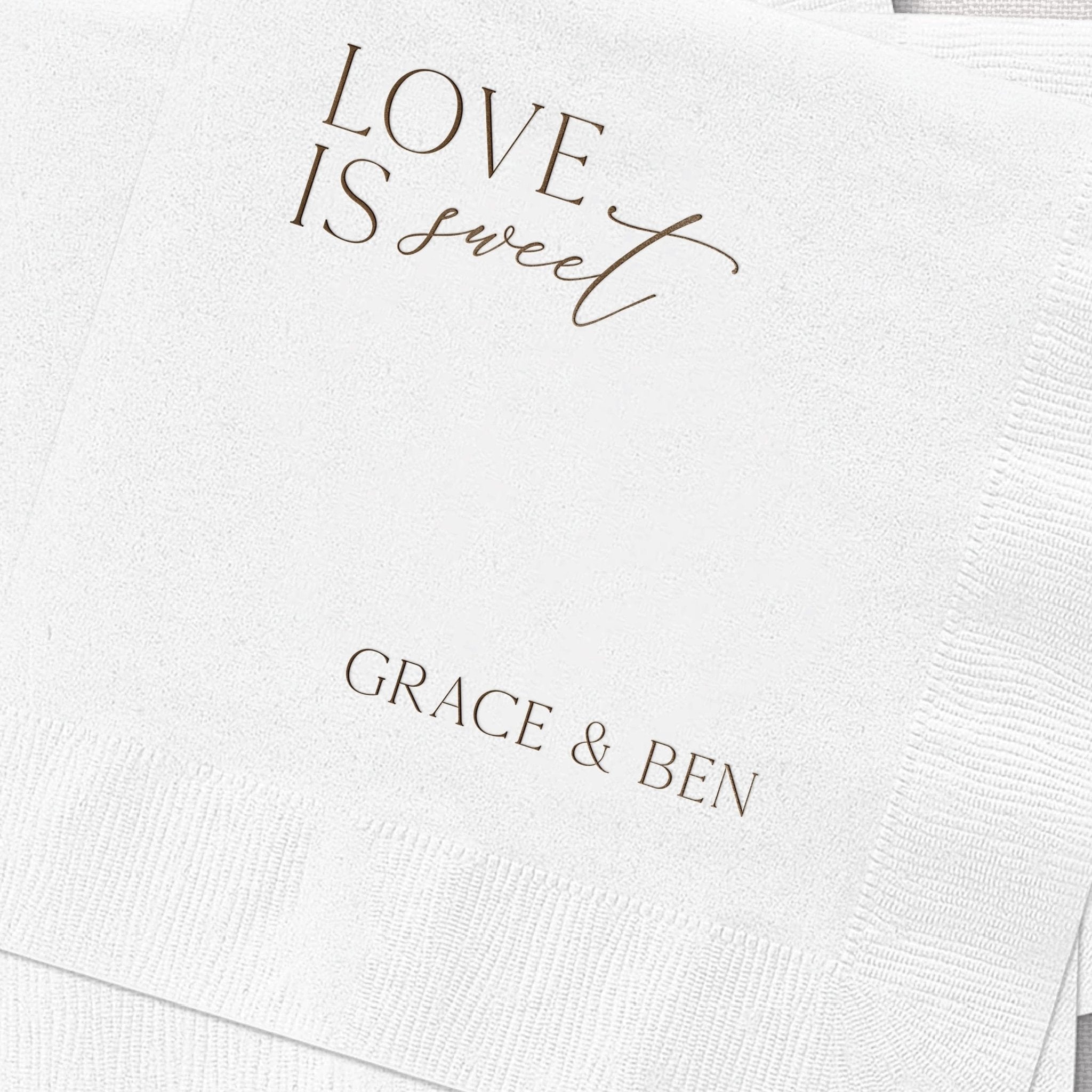 White napkin with gold foil stamped text reading "LOVE IS sweet" and personalized names "GRACE & BEN" below