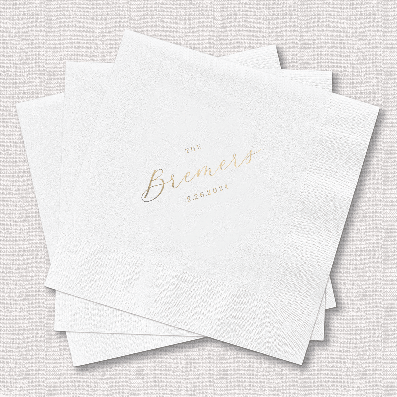 White beverage napkins with gold foil stamped "The Brenners 5.20.23" text design