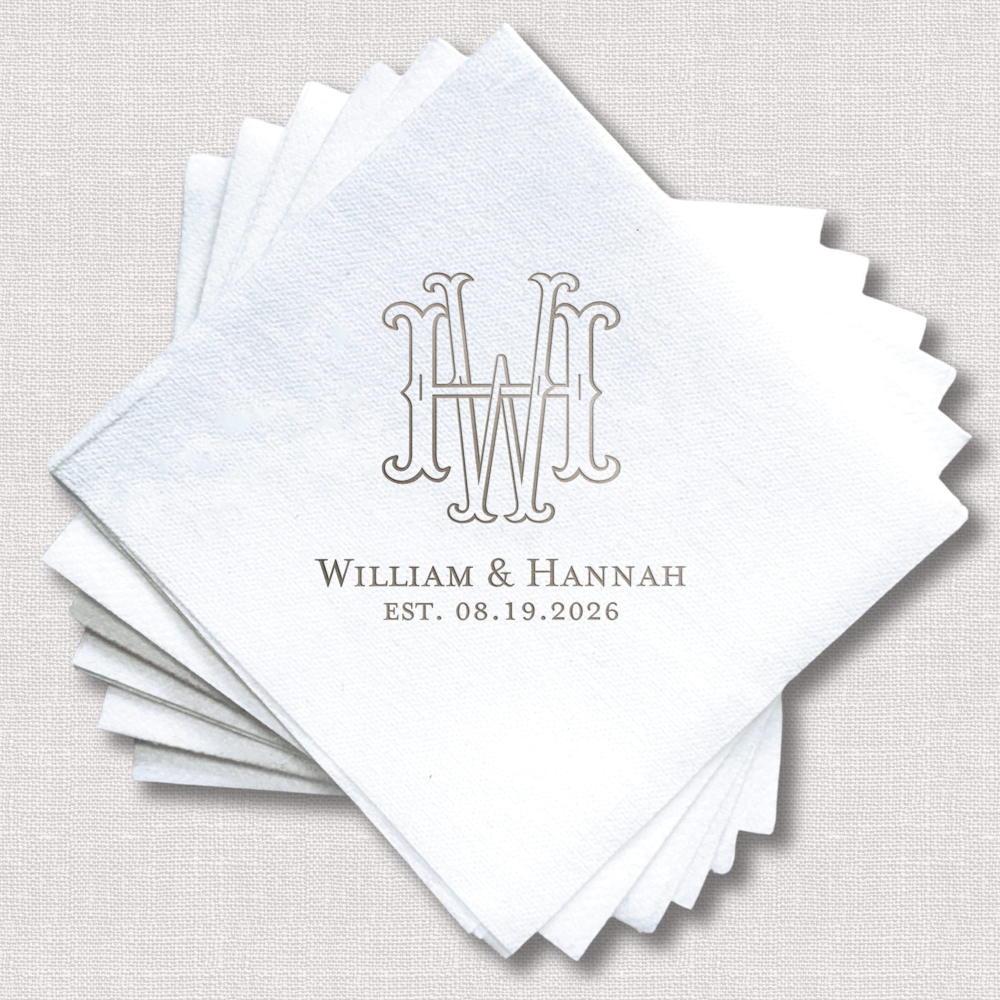 Stack of white linen napkins with interlocking monogram and "William & Hannah EST. 08.19.2026" in gray foil stamping