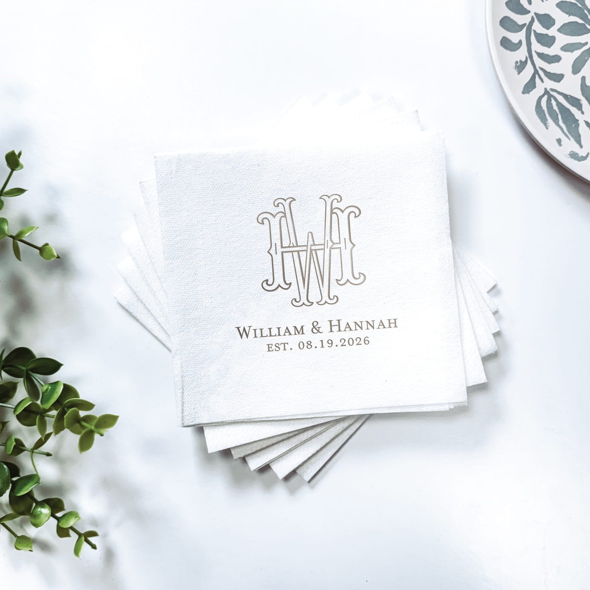 Stack of white linen napkins with interlocking monogram and couple's names and wedding date in foil stamping.