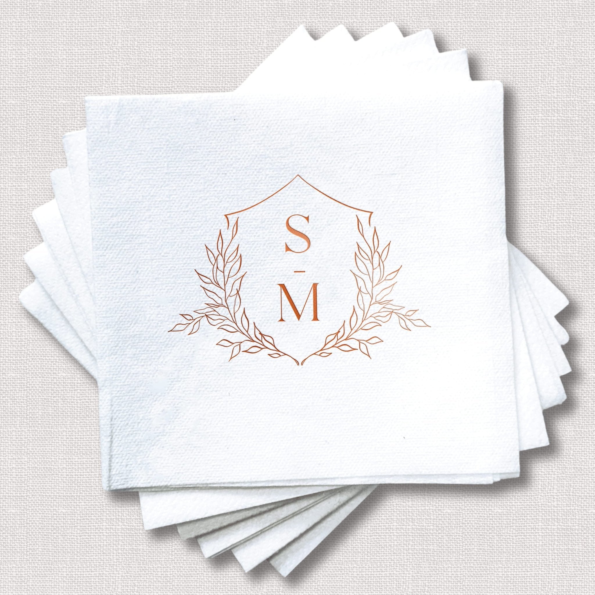 Stack of white linen napkins with copper foil stamped floral crest monogram featuring initials S and M.