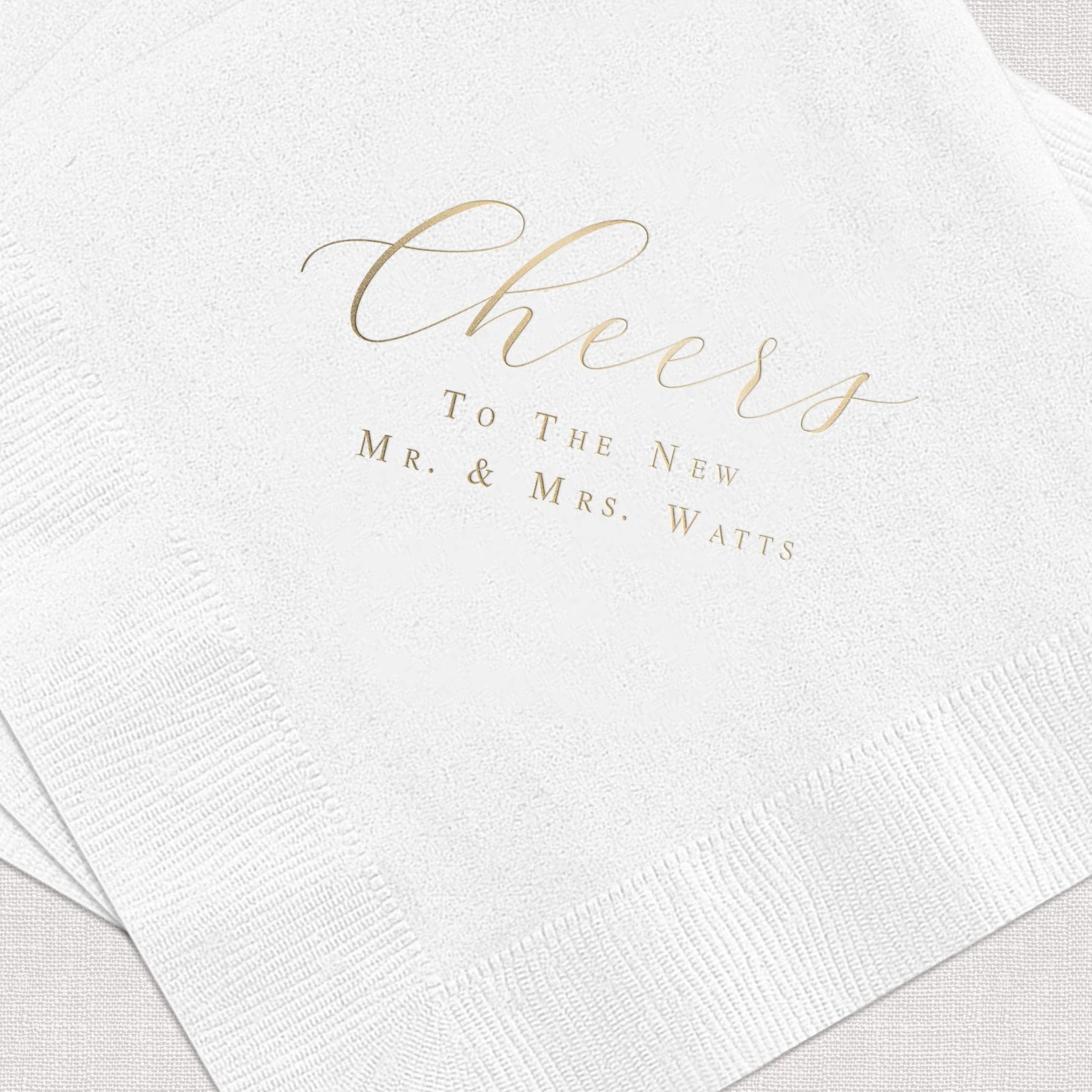 White cocktail napkins with gold foil stamped text reading "Cheers To The New Mr. & Mrs. Watts"