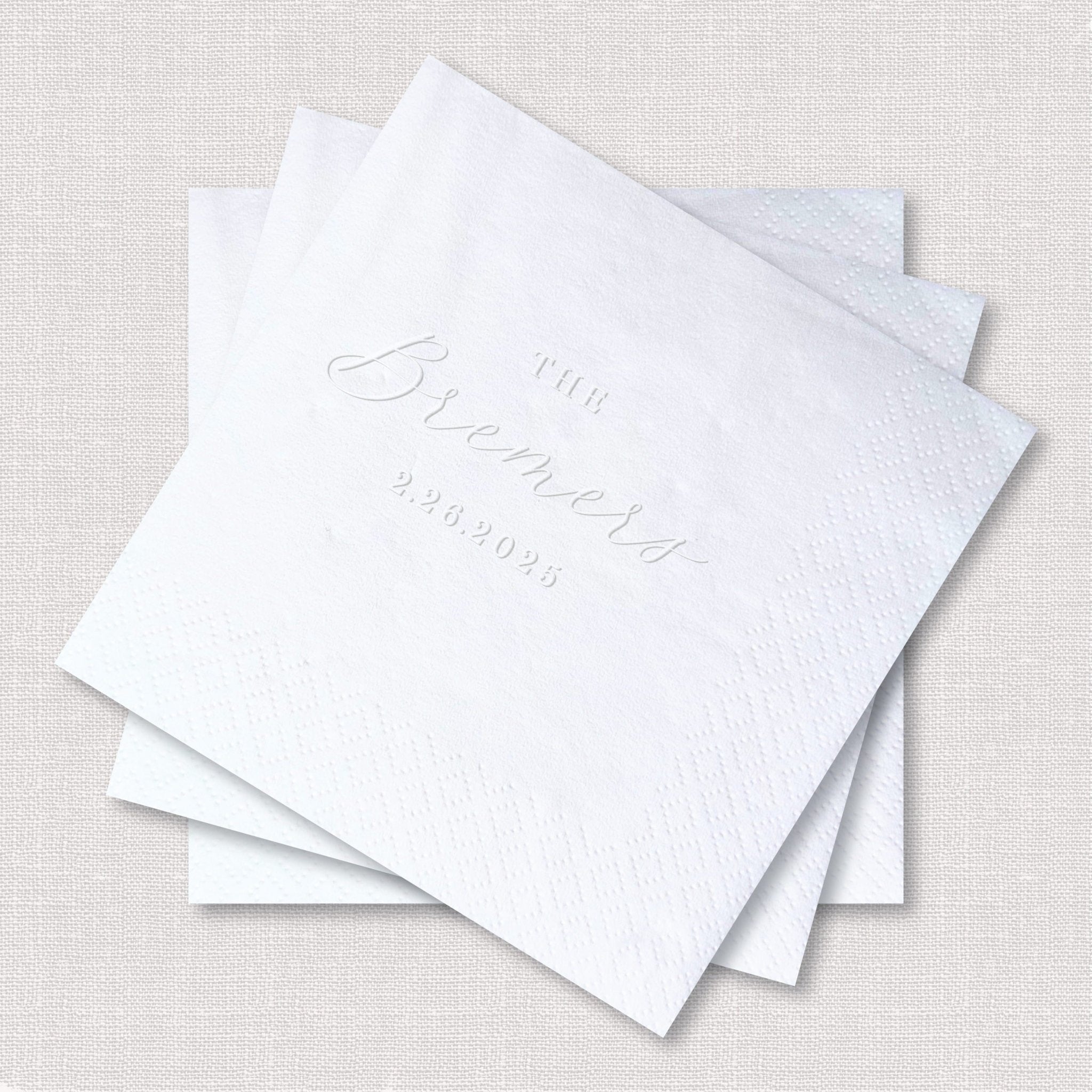 Stack of white embossed napkins with elegant script text reading "Together" and a date, perfect for weddings.