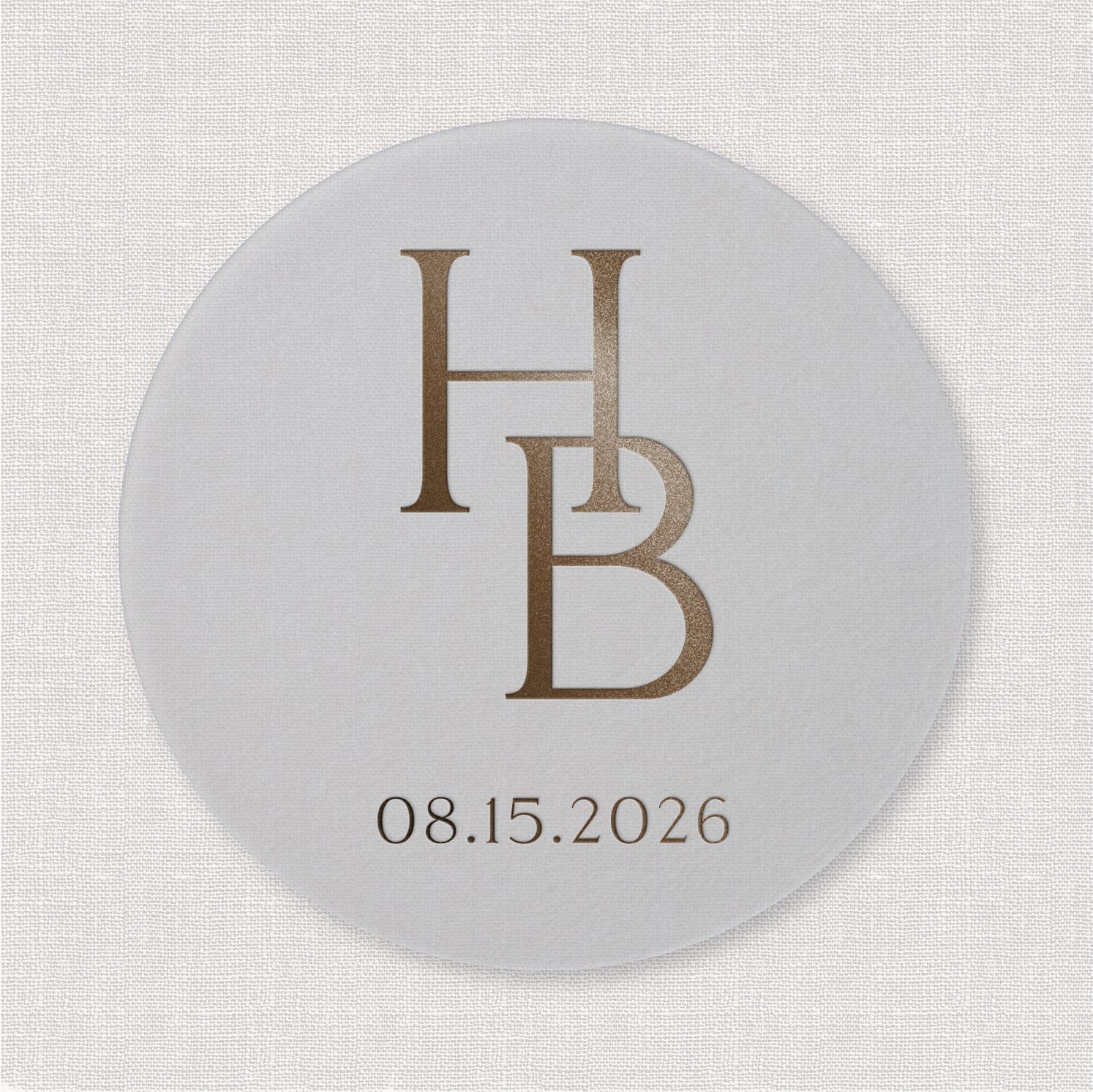 White round coaster with intertwined HB initials and wedding date 08.15.2026 in bronze text