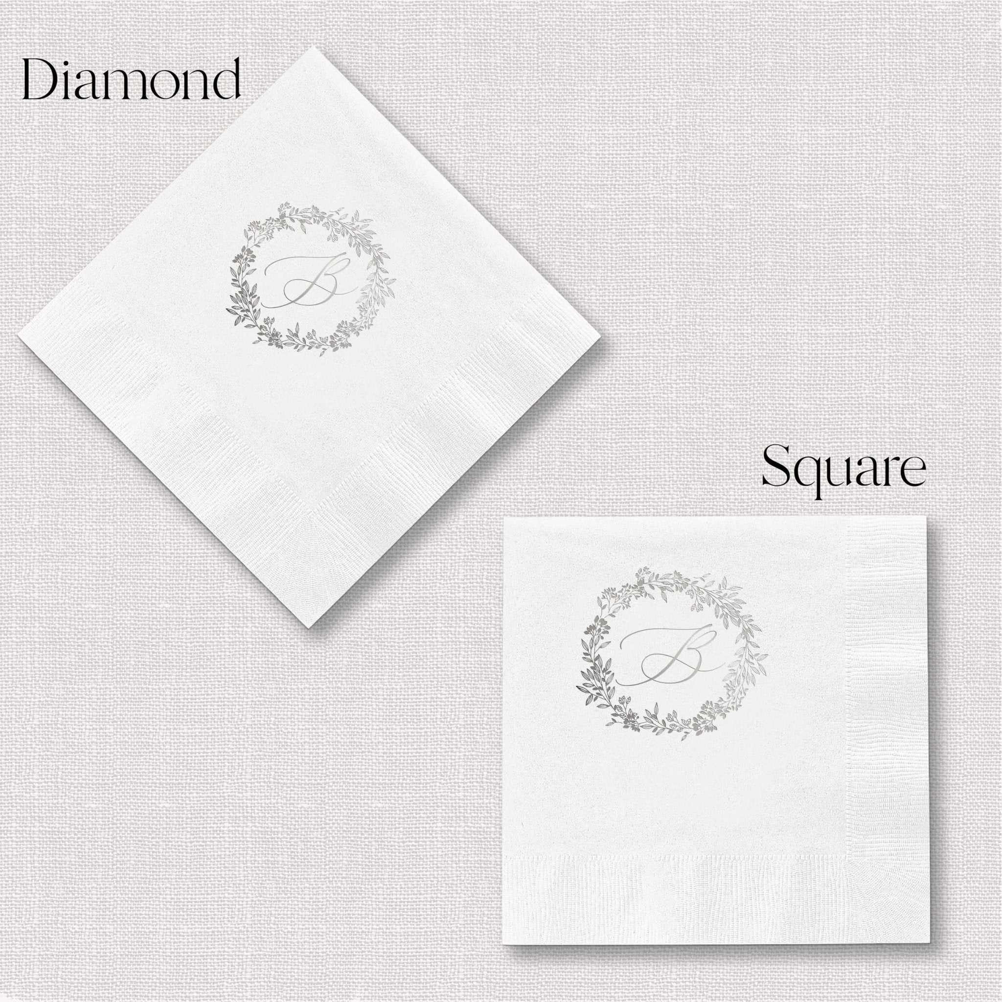 White napkins with diamond and square shapes, each featuring a delicate wreath monogram design in silver foil stamping.