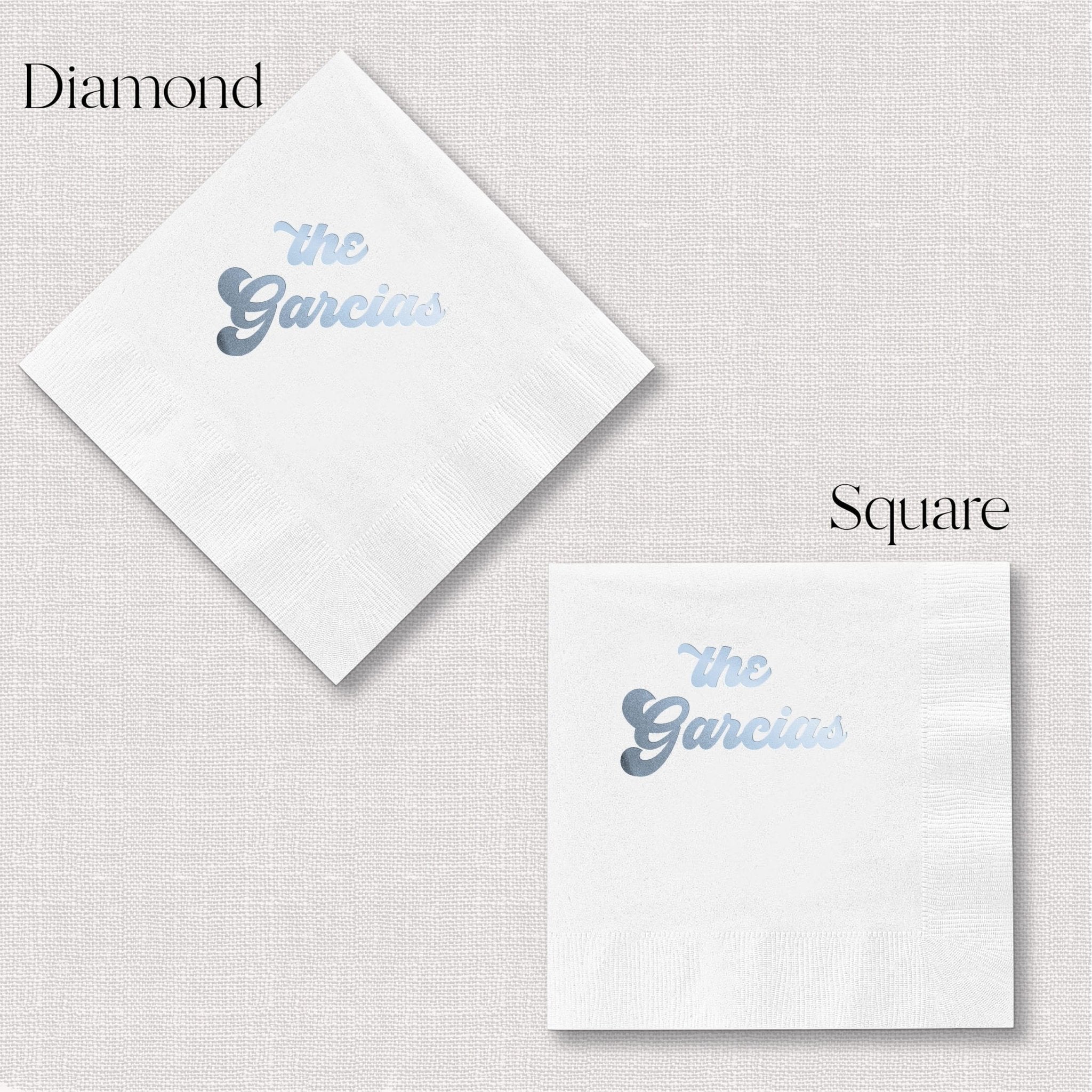White cocktail napkins in diamond and square shapes with "The Garcias" personalized in blue foil stamping.