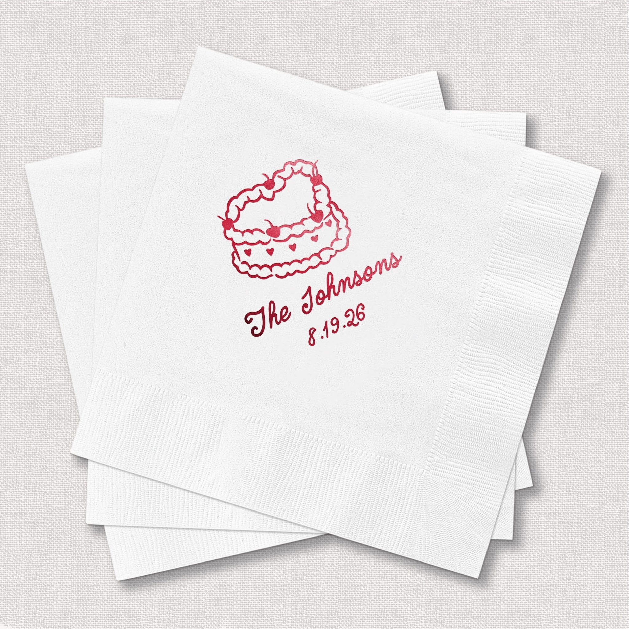 Stack of white cocktail napkins with pink foil-stamped cake design and "The Johnsons 5.19.26" text