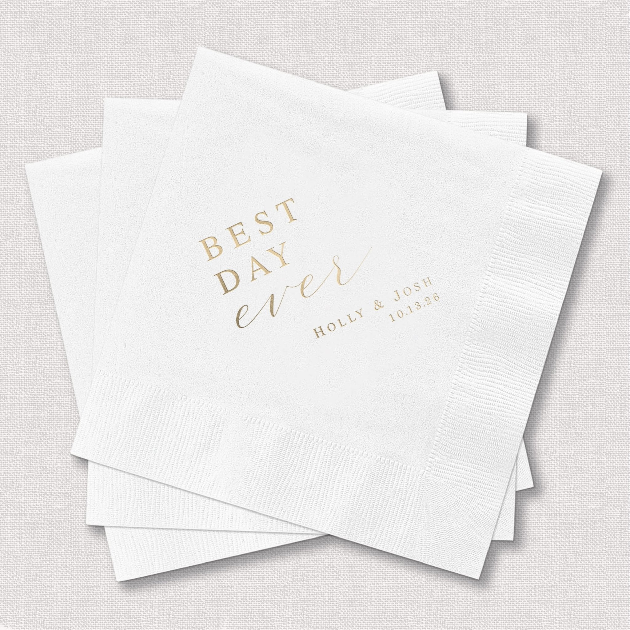 White foil-stamped napkins with "Best Day Ever" in gold script text and personalized names and date below, stacked on white background.