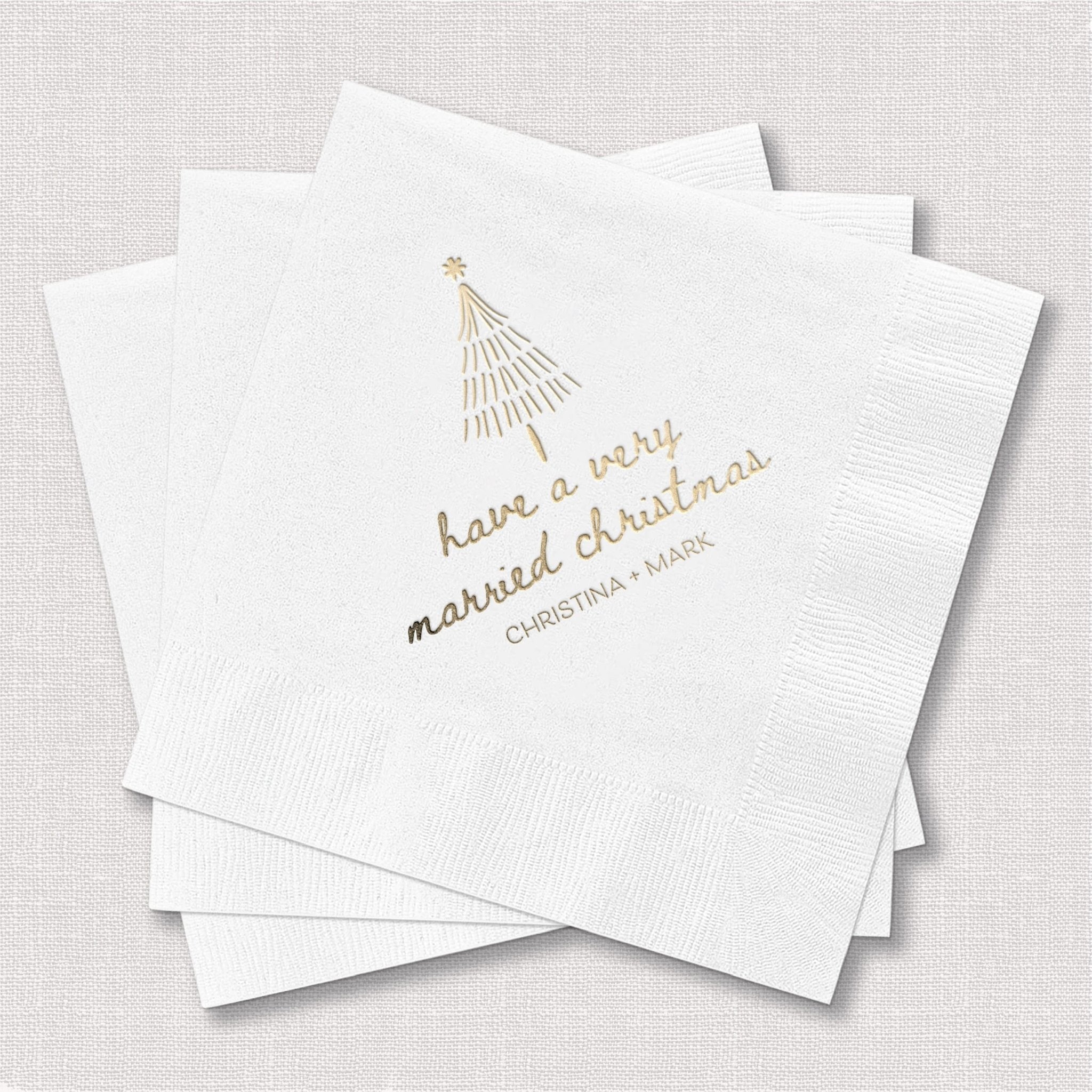 Stack of white napkins with gold foil stamped tree and "have a very married christmas" text with custom names below.