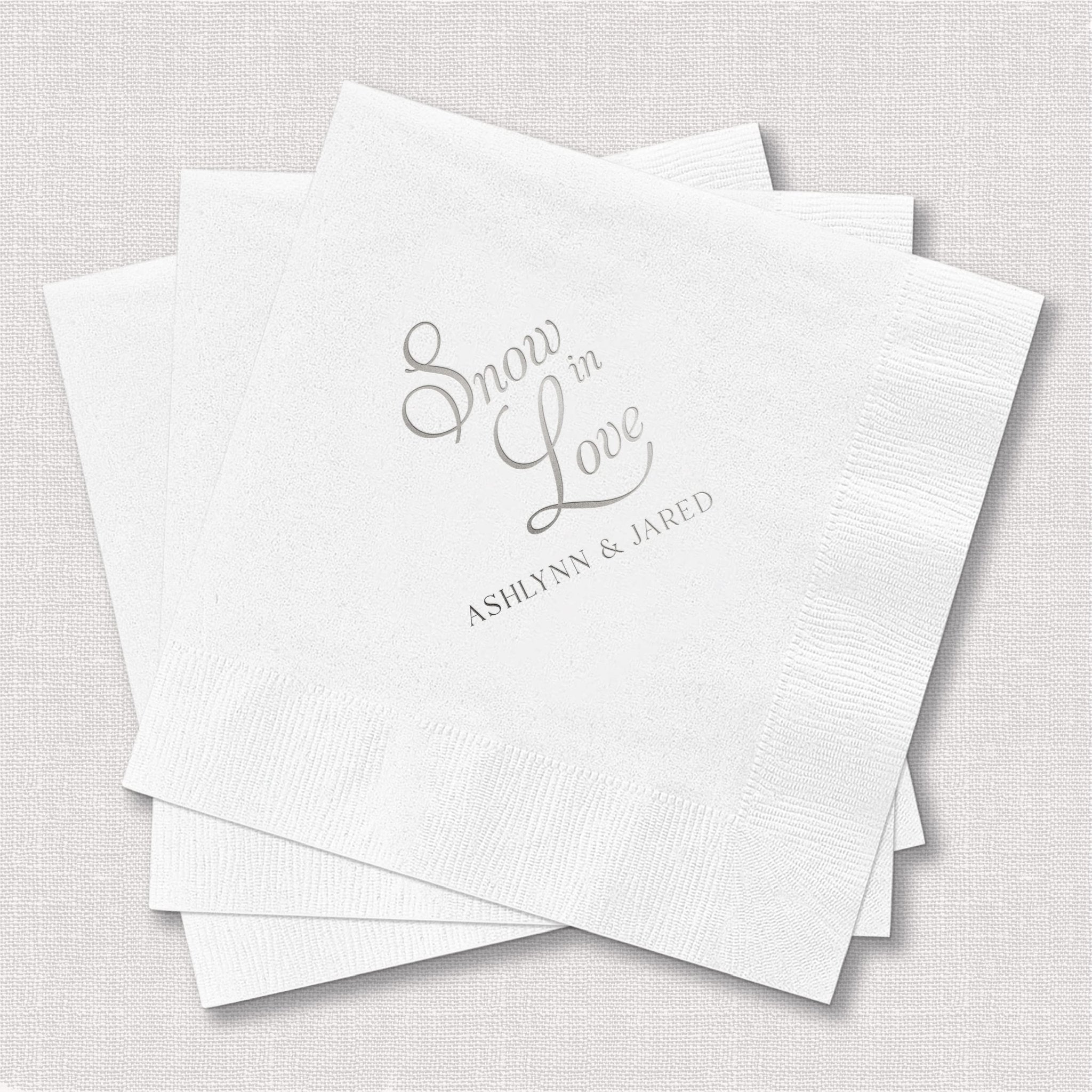 Stack of white napkins with silver foil-stamped "Snow in Love" design and personalized names Ashlyn and Jared