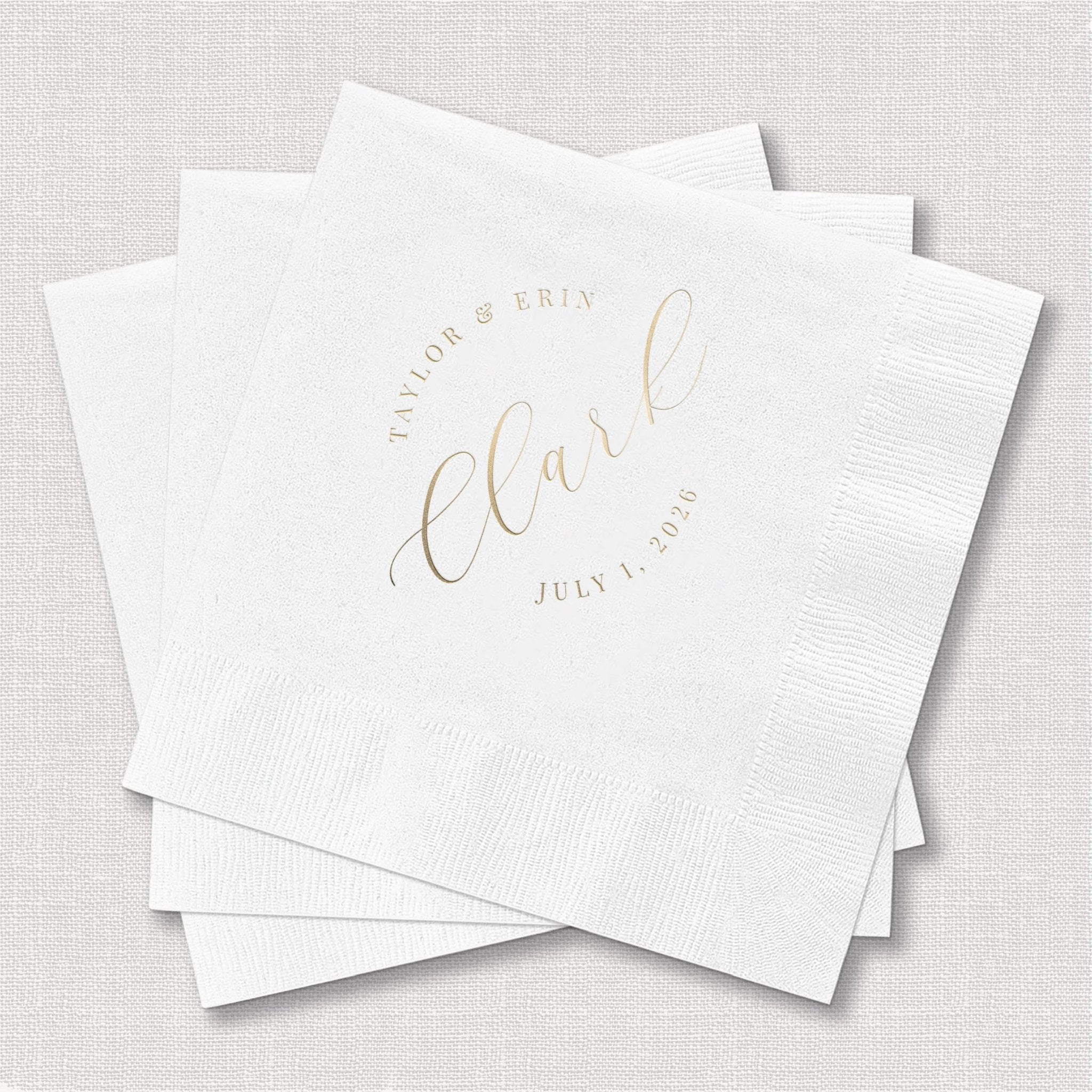Stack of white cocktail napkins with gold foil script reading "Claire" and wedding date personalization.