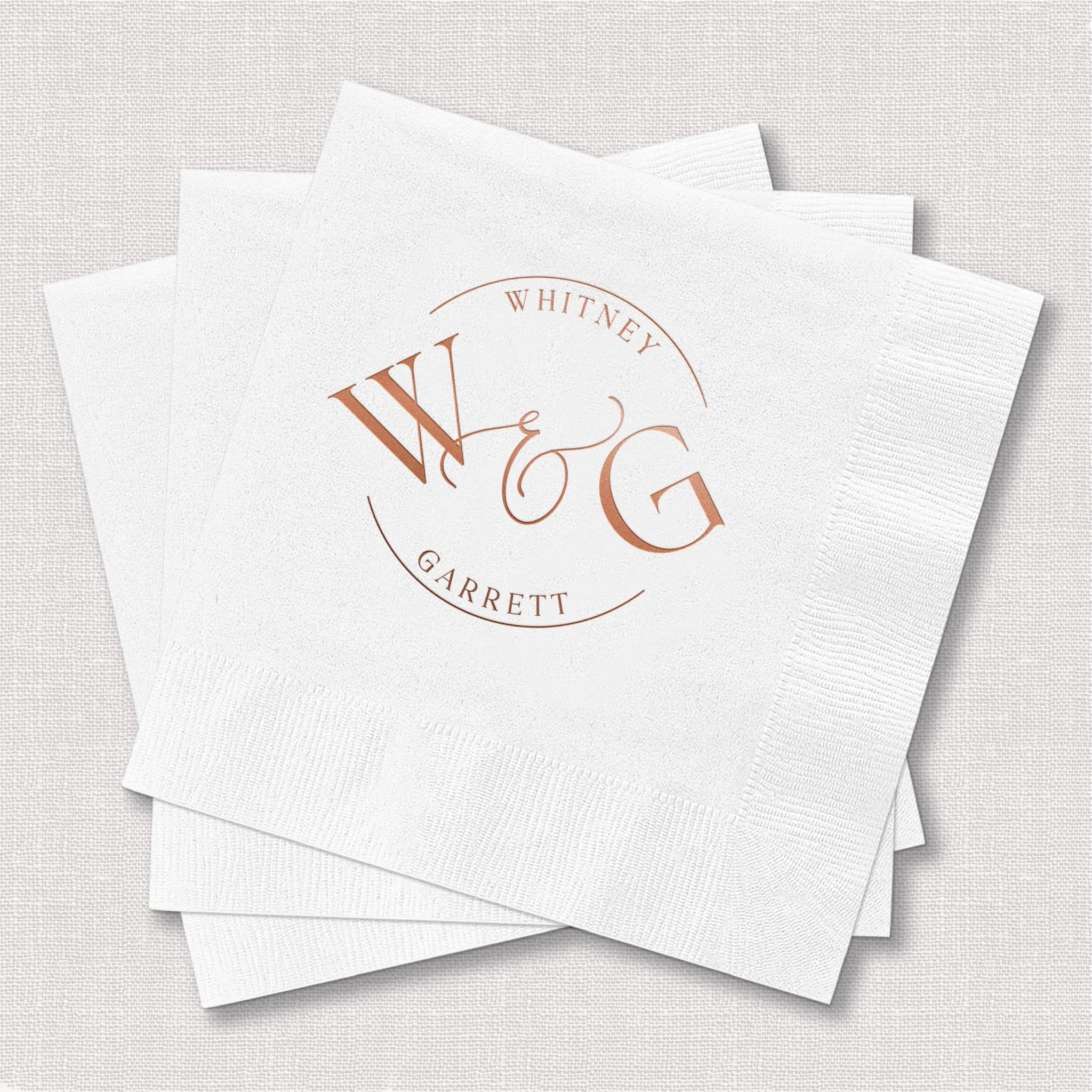 Stack of white napkins with rose gold foil monogram featuring initials WMG in circular wreath design with couple names Whitney and Garrett