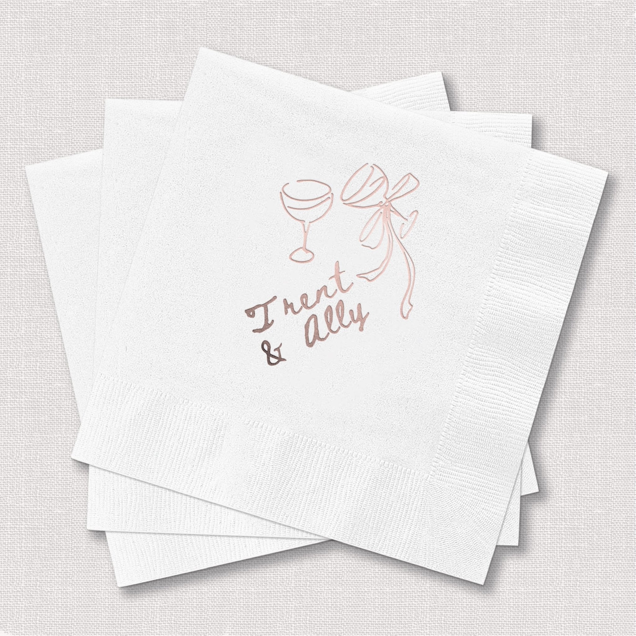 White cocktail napkins with rose gold foil design of champagne glasses, ribbon bow, and "Toast & Ally" text