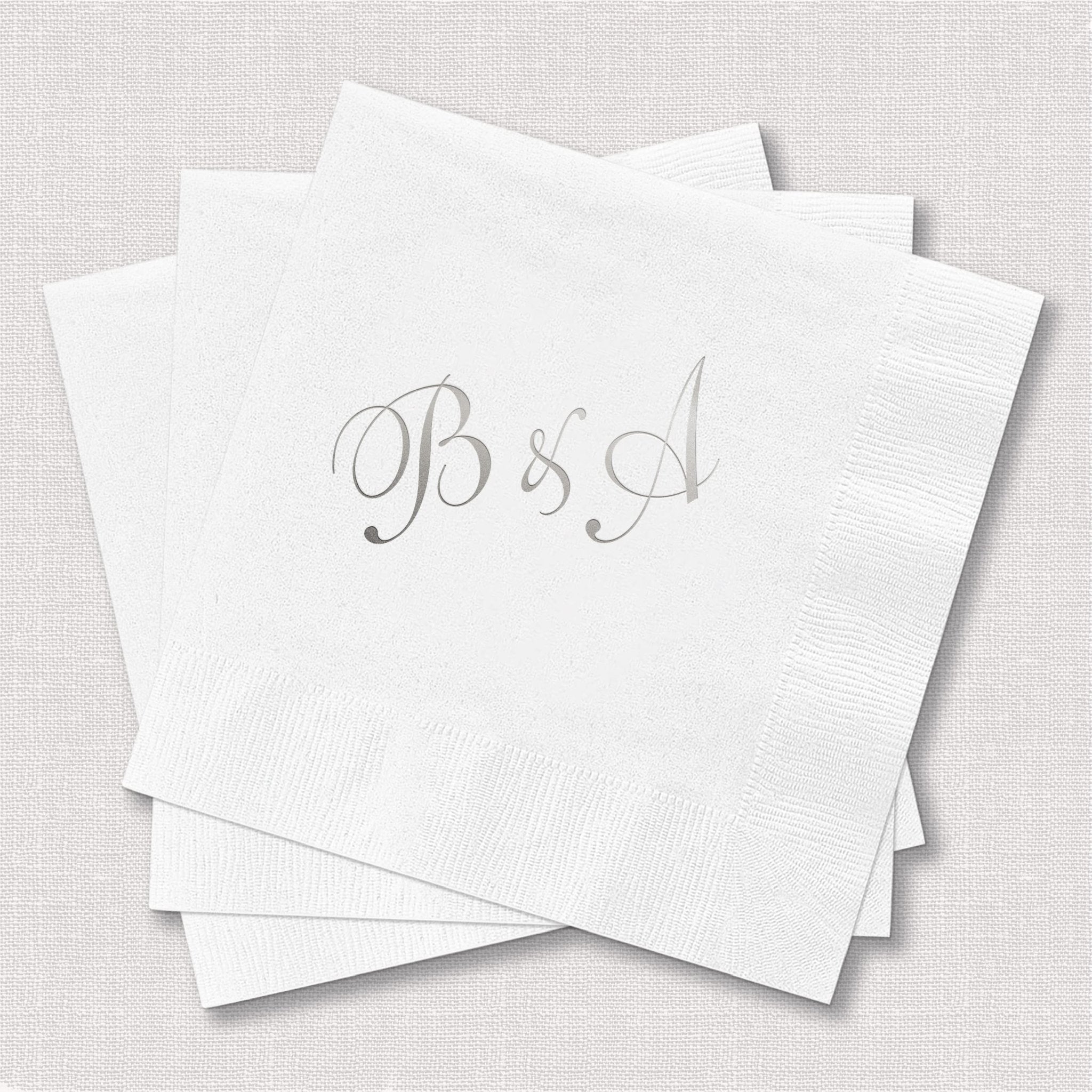 Stack of white napkins with silver foil-stamped monogram initials B and J in elegant script