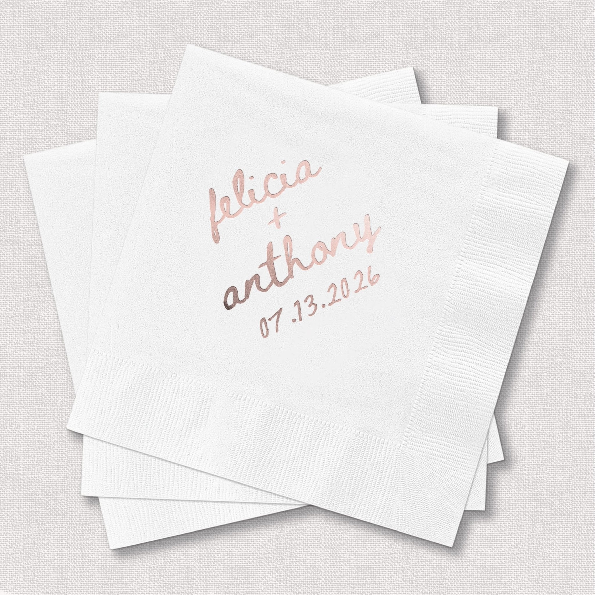 Stack of white cocktail napkins with "felicia + anthony" and date "07.13.2024" in rose gold foil stamping.