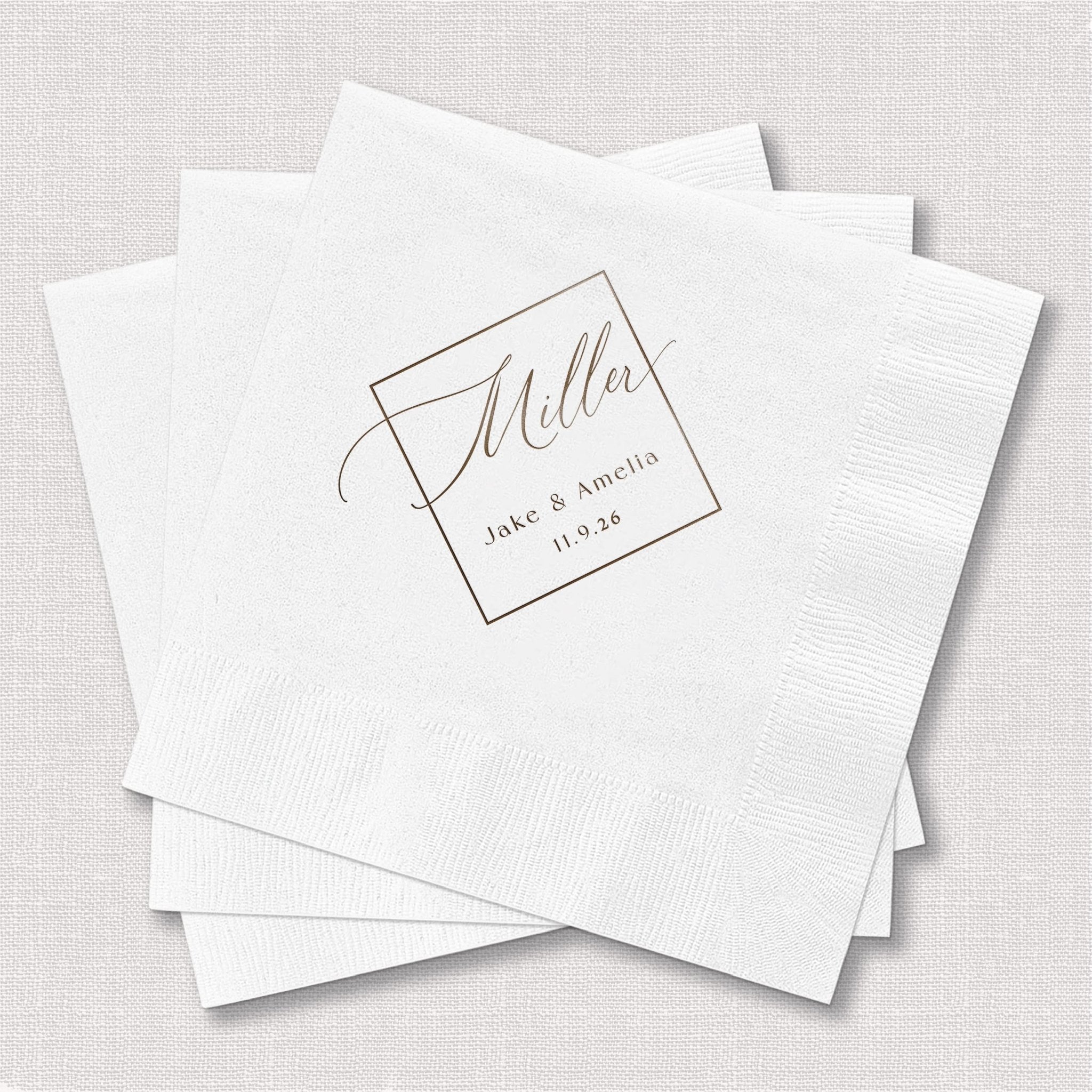 Stack of white square napkins with elegant script monogram and names "James & Amelia" with wedding date personalization in foil stamped design.