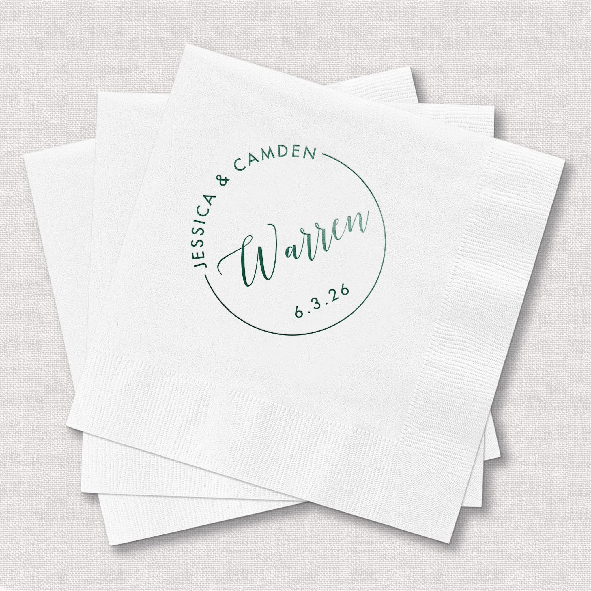 Stack of white personalized napkins with blue foil-stamped circle monogram featuring names "Jessica & Camden," "Warren," and date "6.3.26"