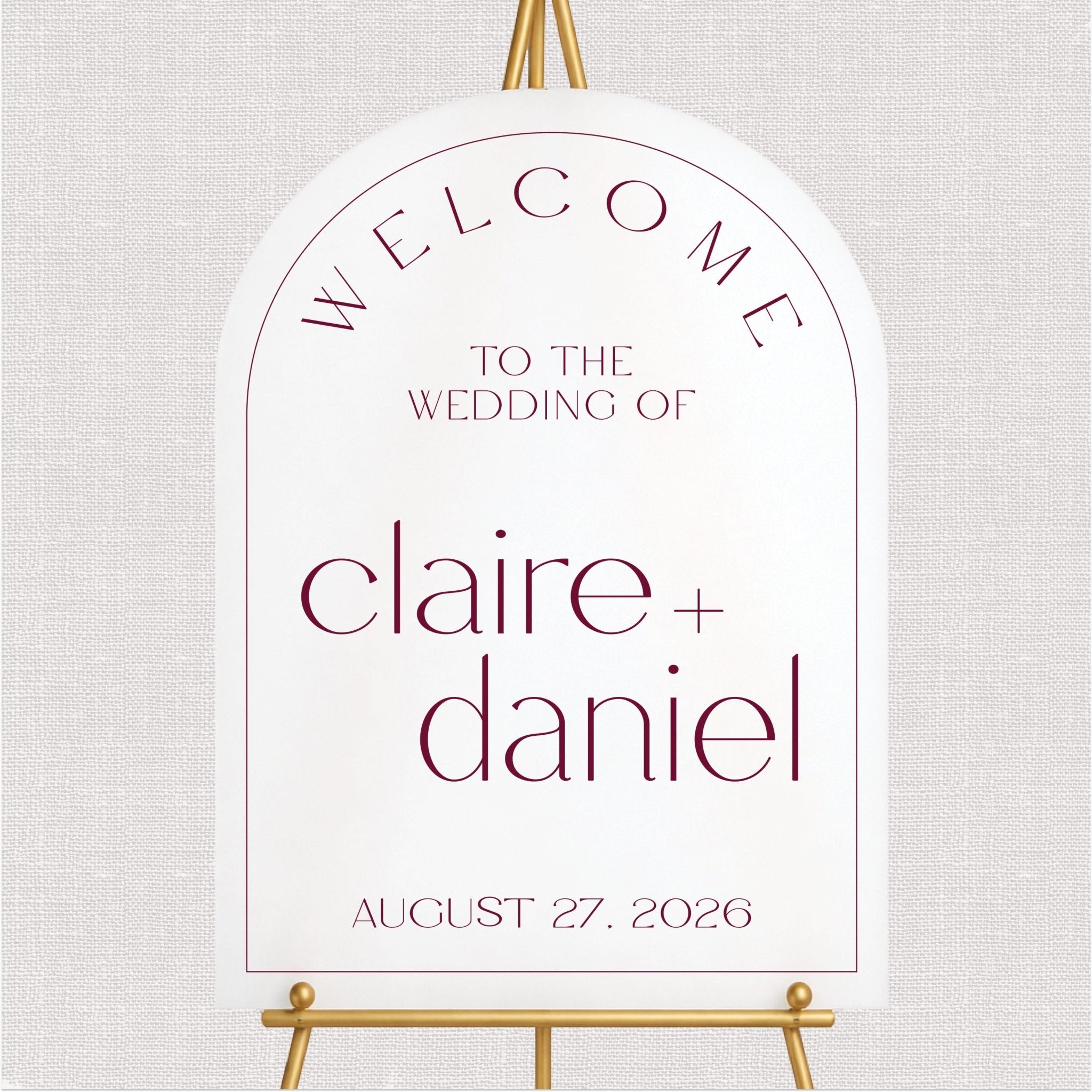 White arch welcome sign with burgundy personalized wedding text and gold easel stand