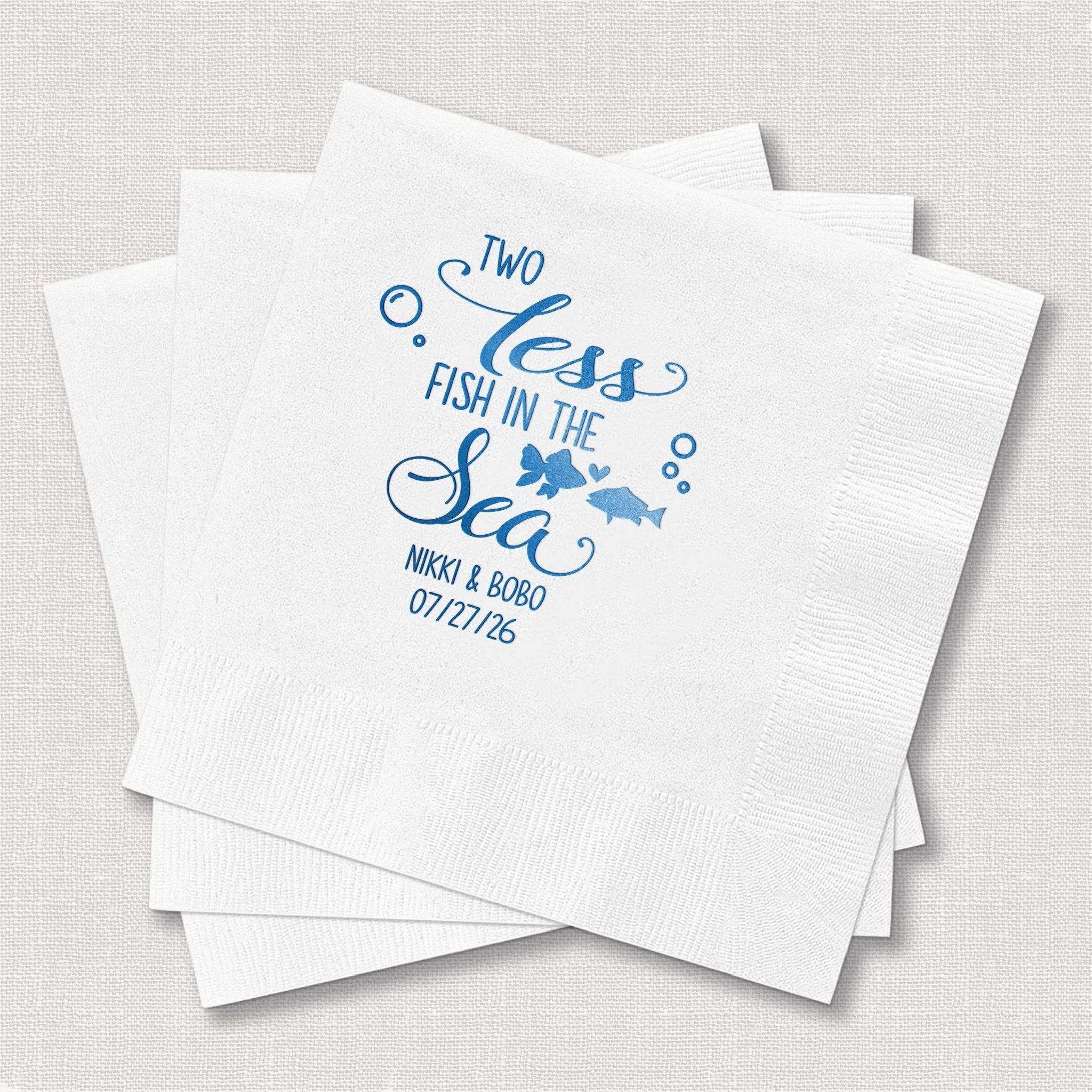 White napkins with blue foil stamped design reading "Two Less Fish in the Sea" with fish graphics and personalized names and date.
