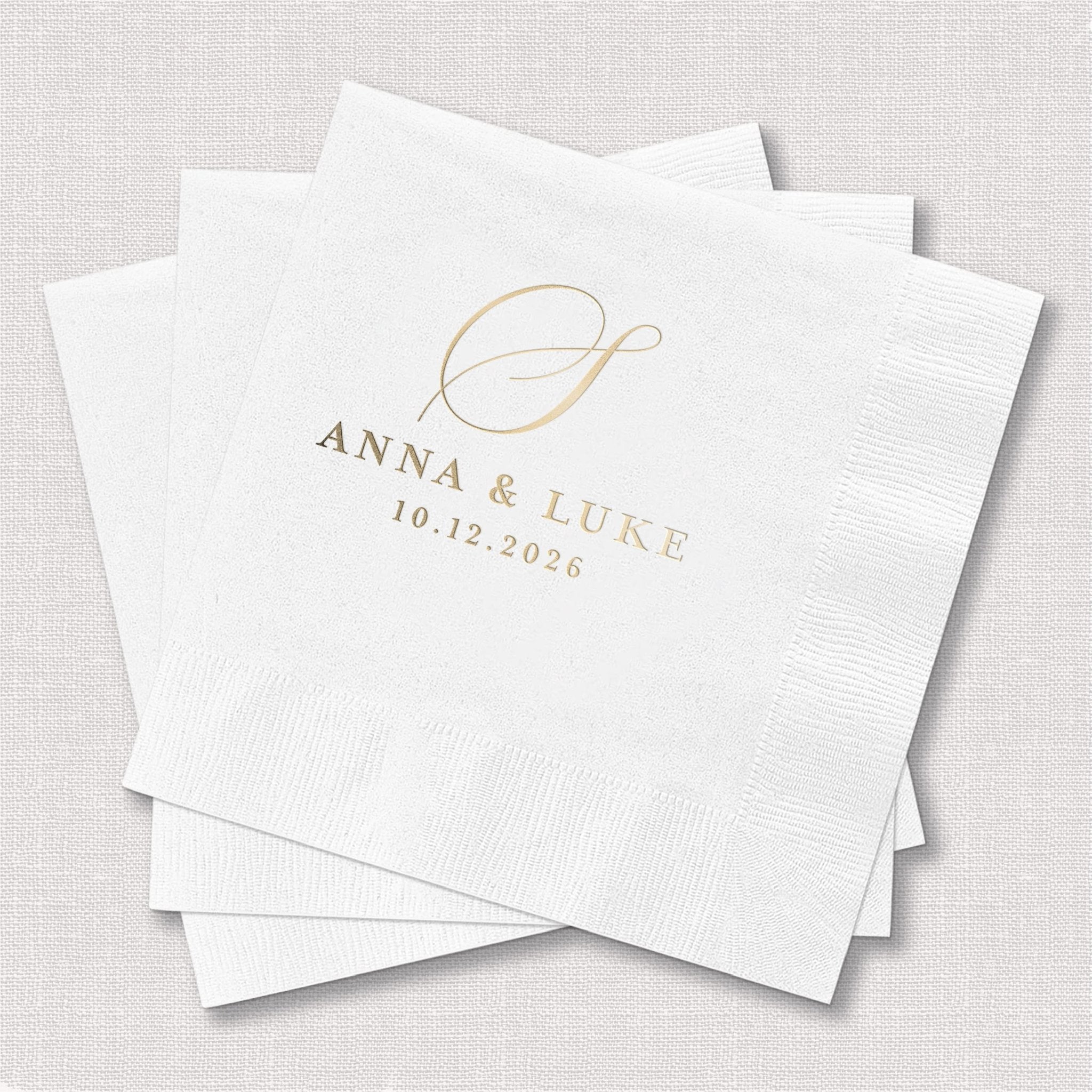 White cocktail napkins with gold foil monogram and names "Anna & Luke" with wedding date 10.12.2025