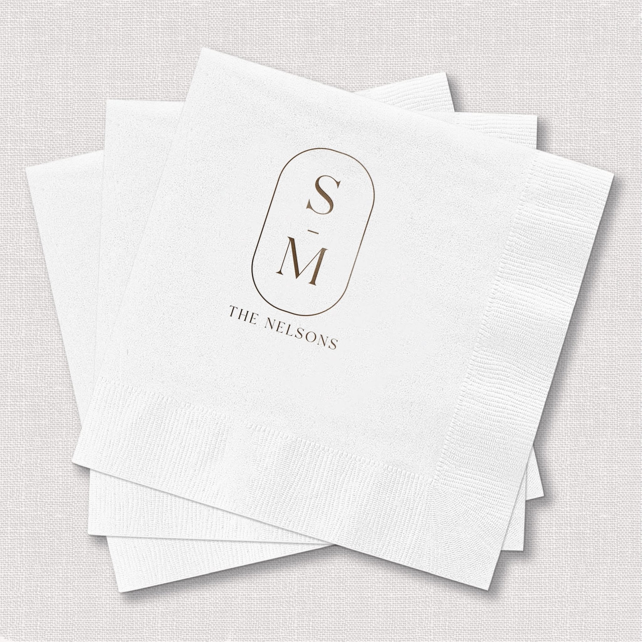 Stack of white cocktail napkins with foil-stamped monogram SM and "THE NELSONS" text