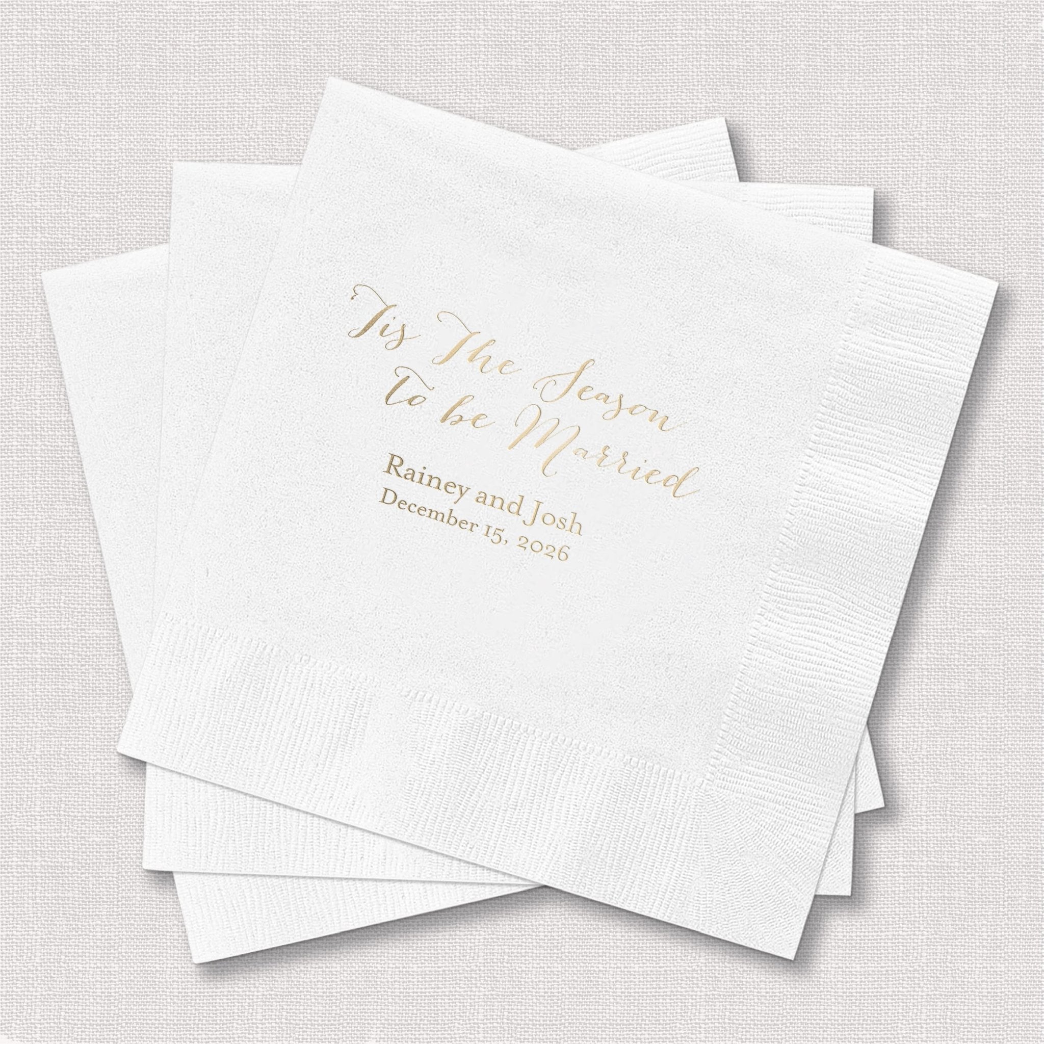 Stack of white cocktail napkins with gold foil text reading "Tis the Season to be Married" and personalized names and date.