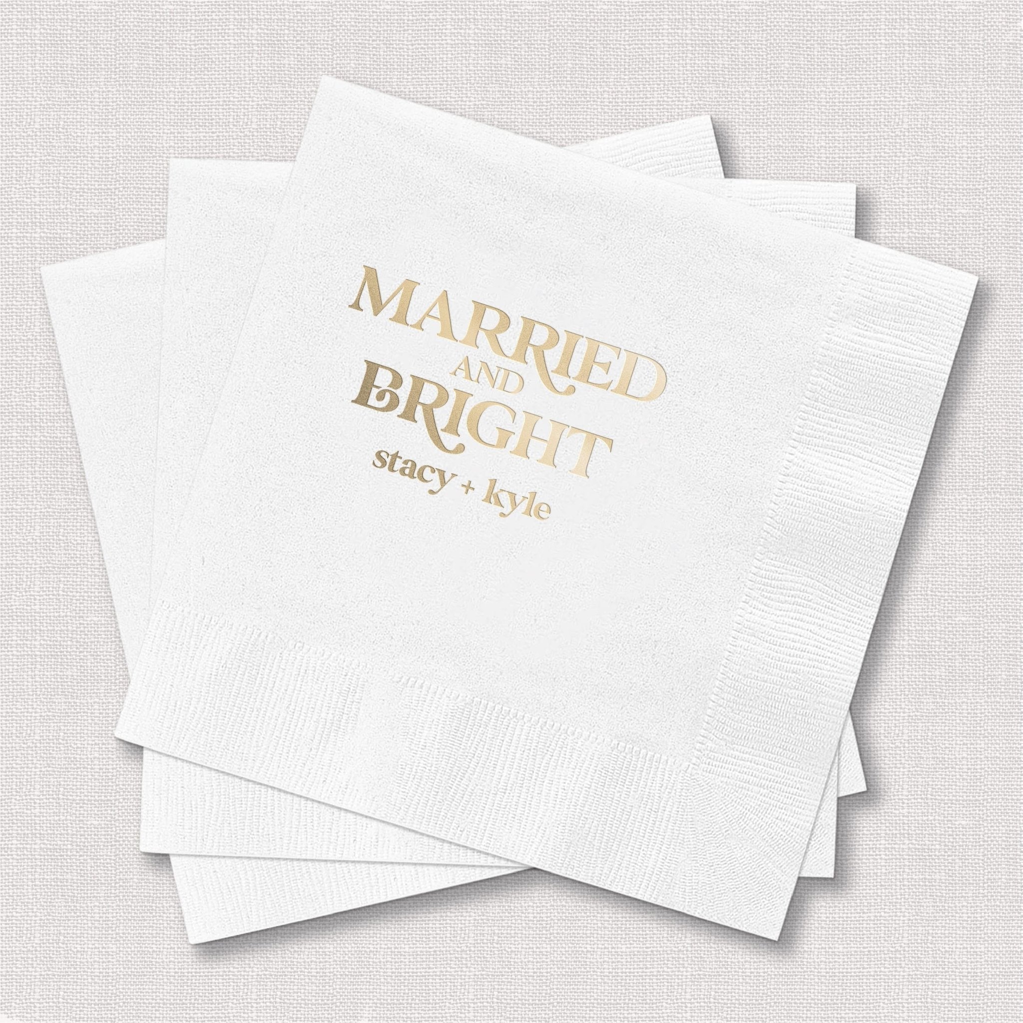 White napkins with gold foil stamped text reading "Married and Bright" and personalized names "stacy + kyle"