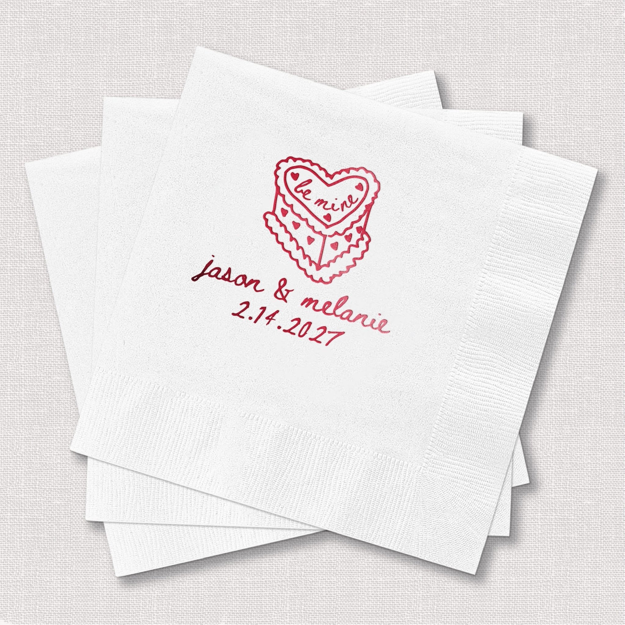 Stack of white napkins with red foil-stamped lace heart design and personalized names "jason & melanie" with wedding date 2.14.2027.