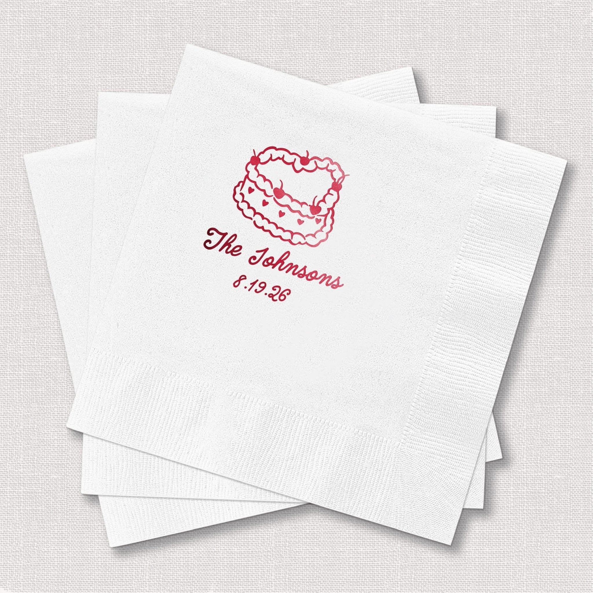White cocktail napkins with red foil-stamped cake design and personalized text reading "The Johnsons 8.19.28"