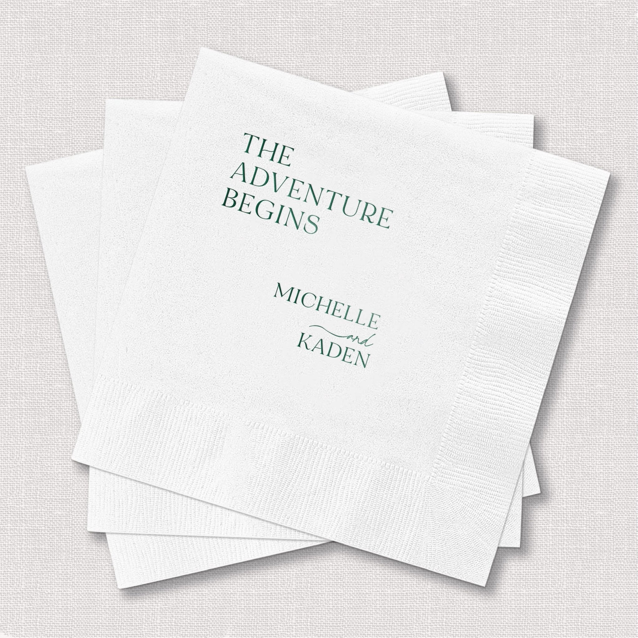 White beverage napkins with "The Adventure Begins" and names Michelle and Kaiden printed in teal foil lettering.
