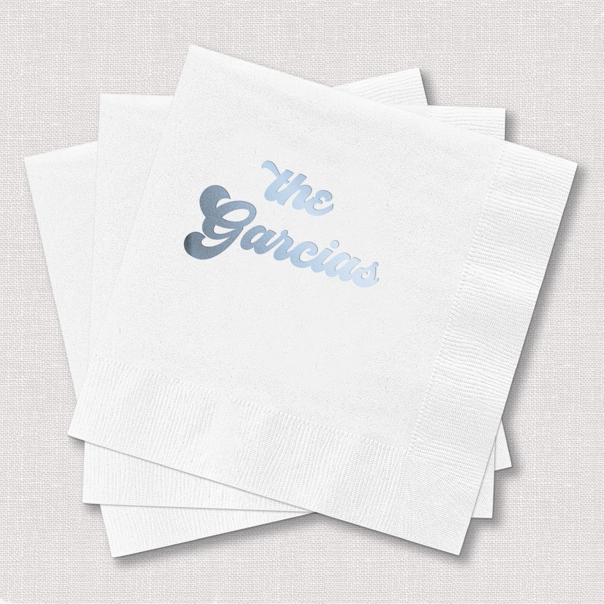 Stack of white cocktail napkins with light blue foil-stamped text reading "The Garcias"