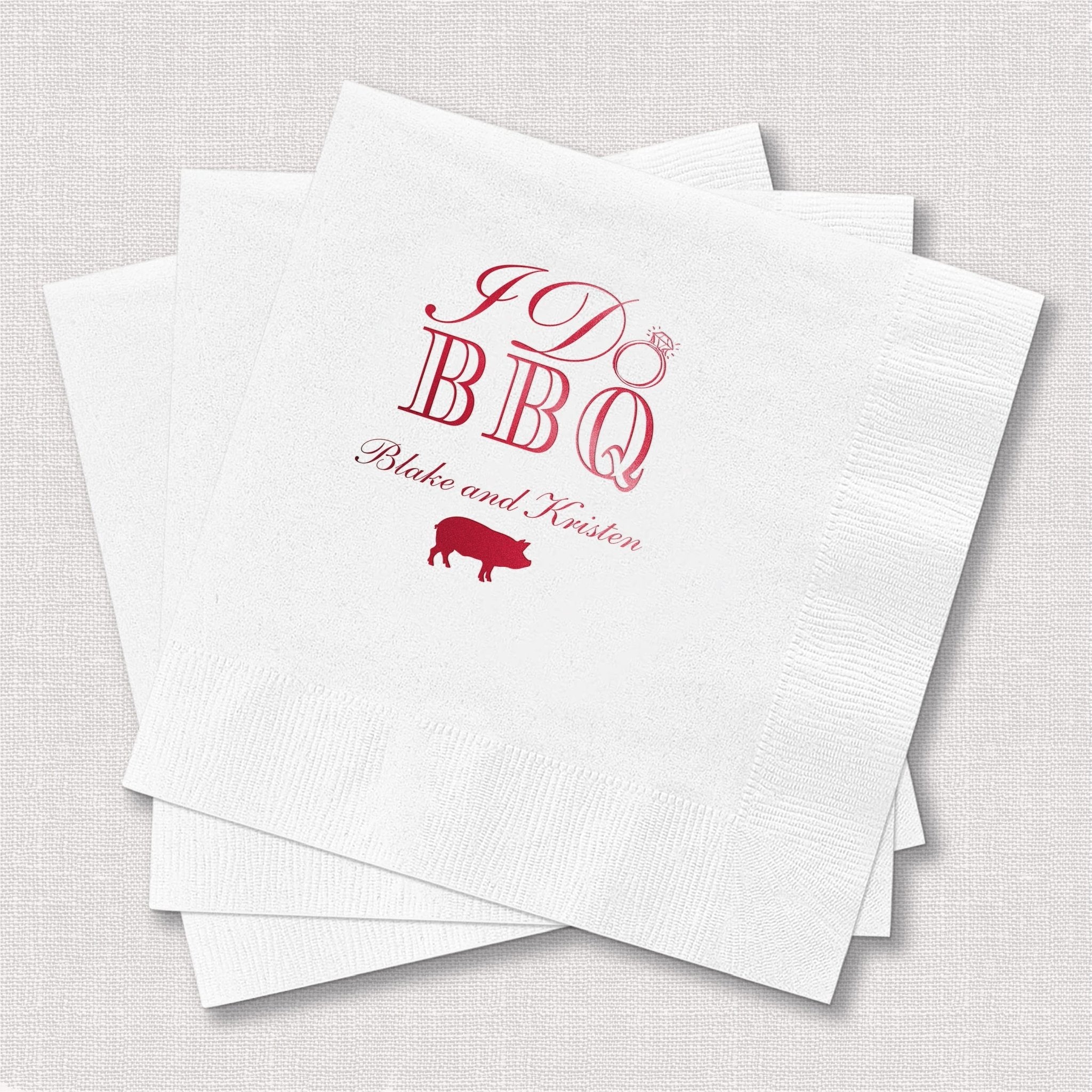Stack of white napkins with burgundy foil-stamped I Do BBQ design, pig icon, and personalized names Blake and Keston.