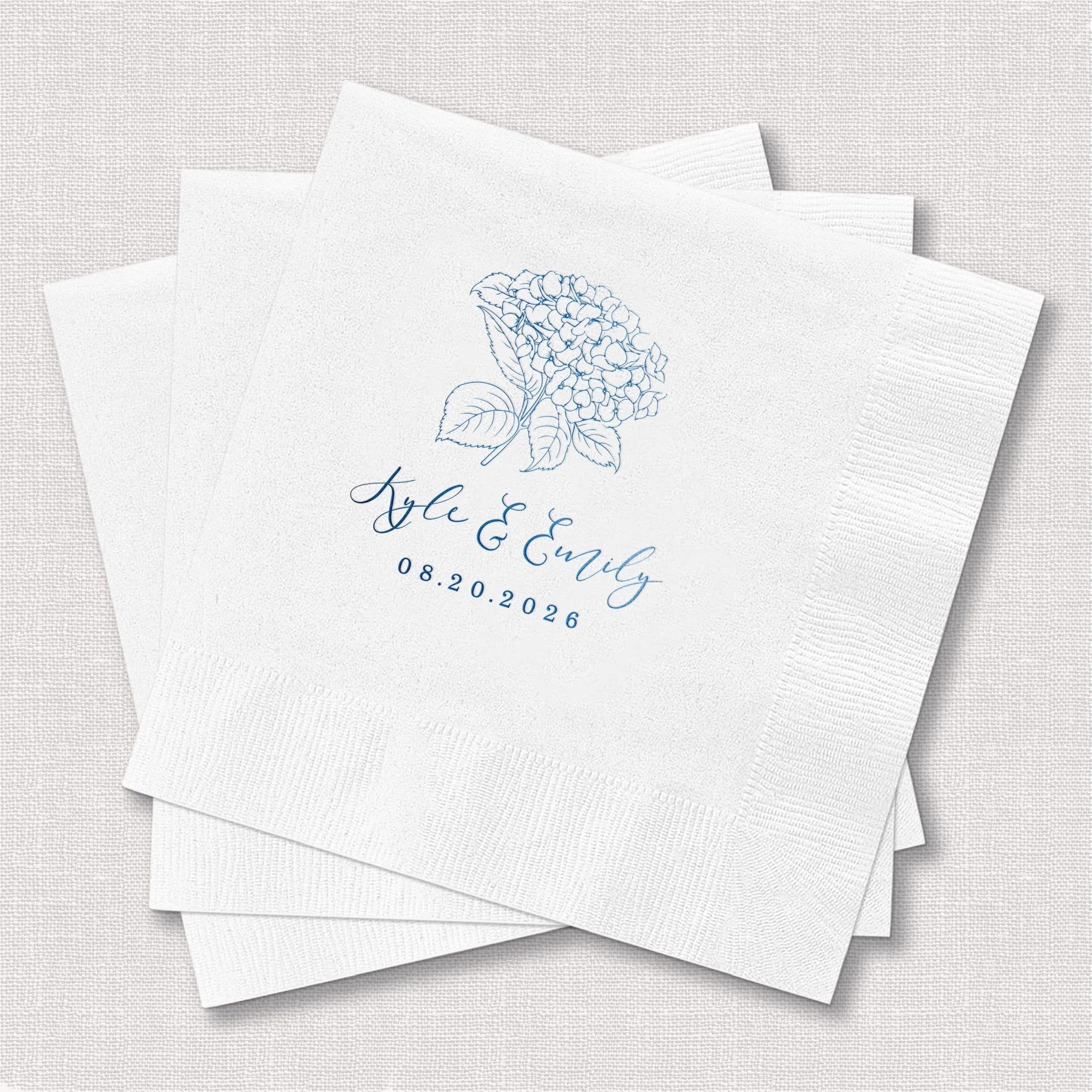 White napkins with blue foil-stamped hydrangea design and "love grows" text with wedding date.