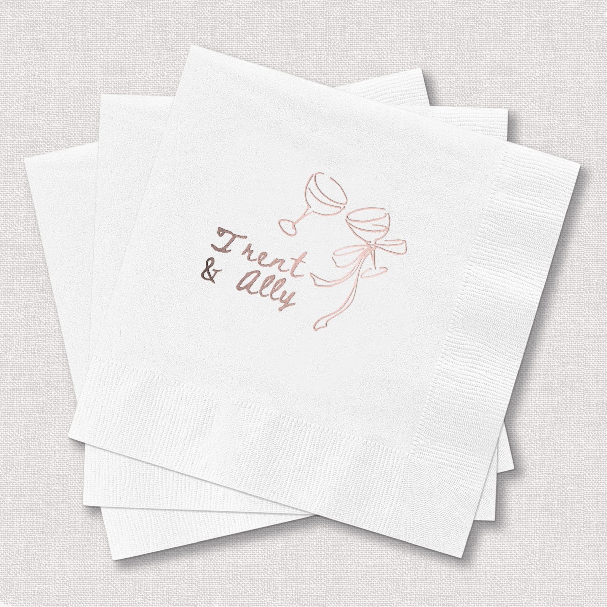 Stack of white paper napkins with rose gold foil-stamped design featuring champagne glasses and "Toast & Elly" text.