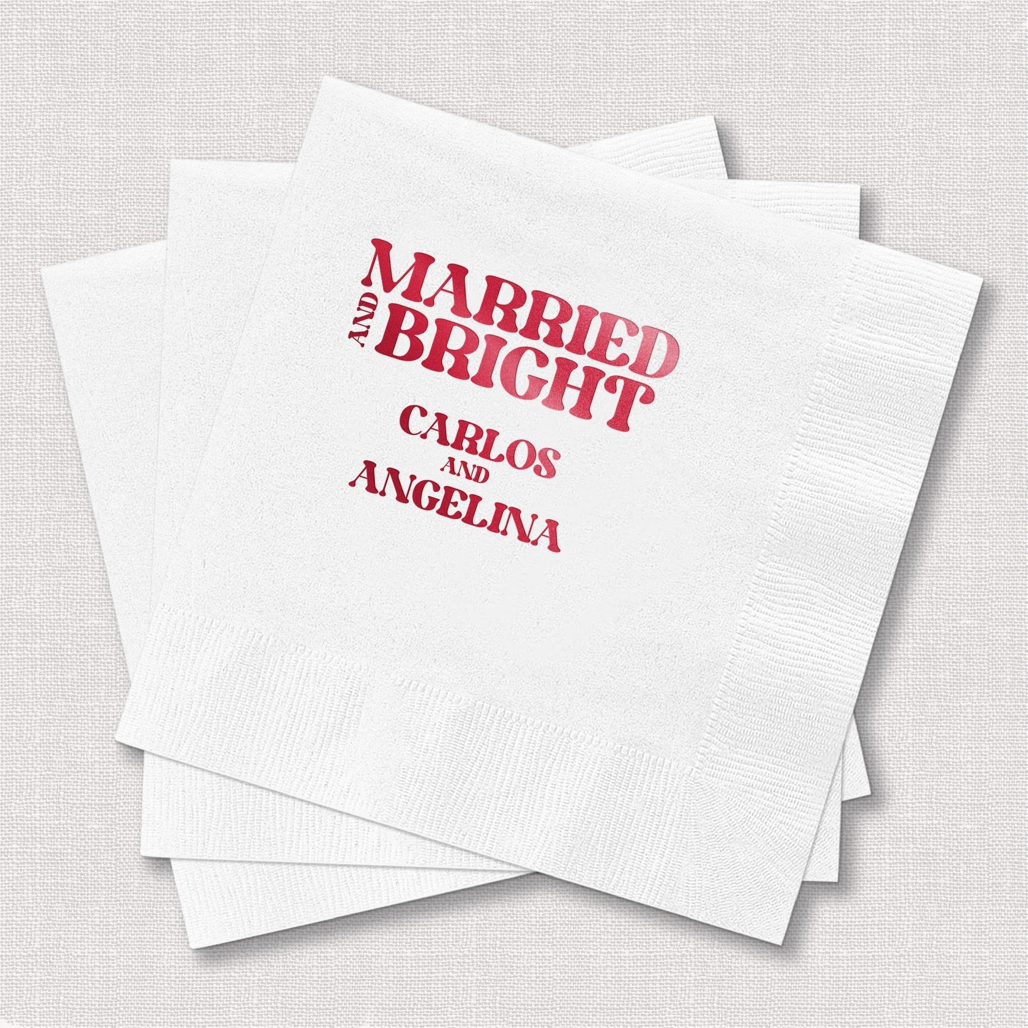 Stack of white napkins with pink foil-stamped text reading "Married and Bright" with personalized names Carlos and Angelina below.