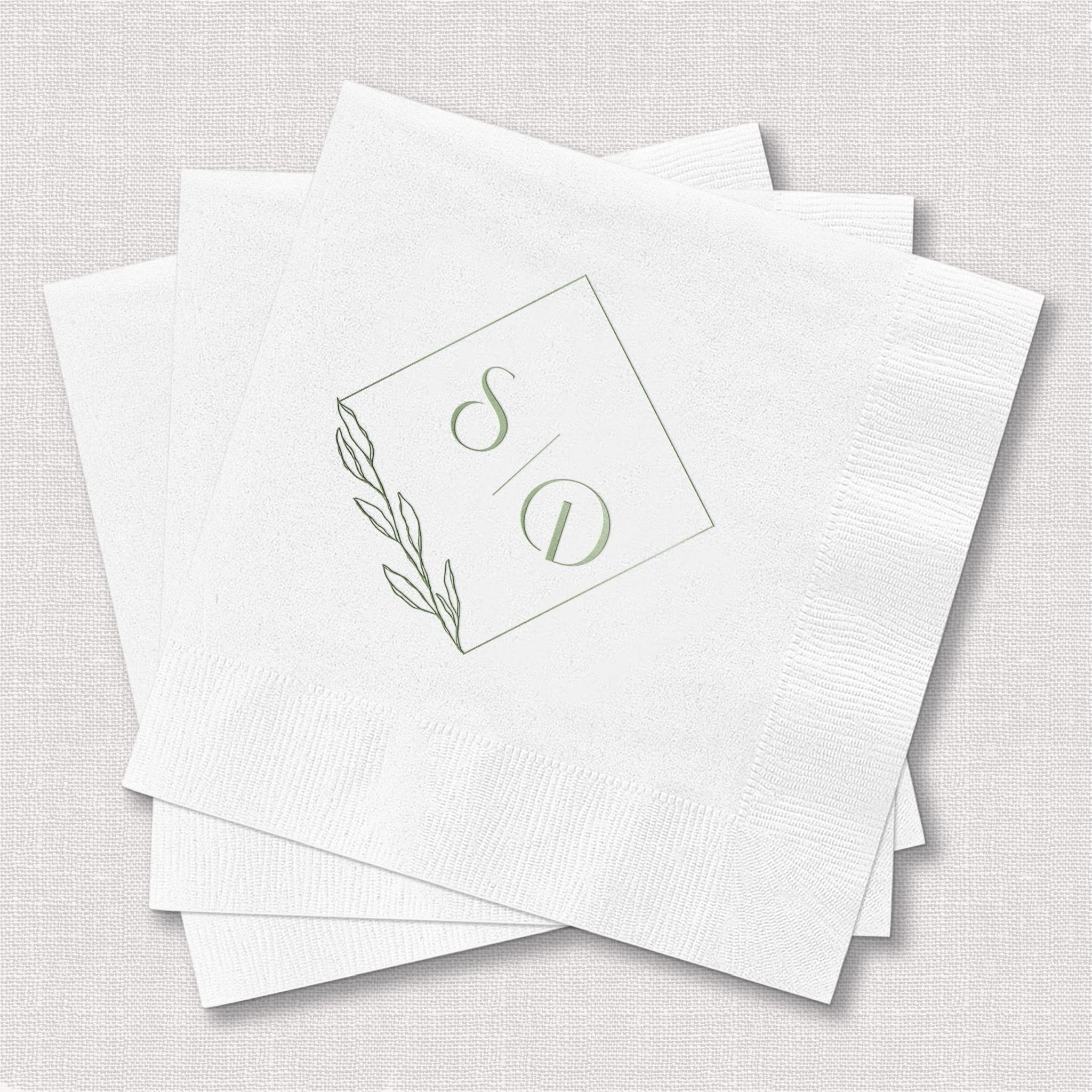 Stack of white napkins with gold foil monogram design and botanical leaf detail