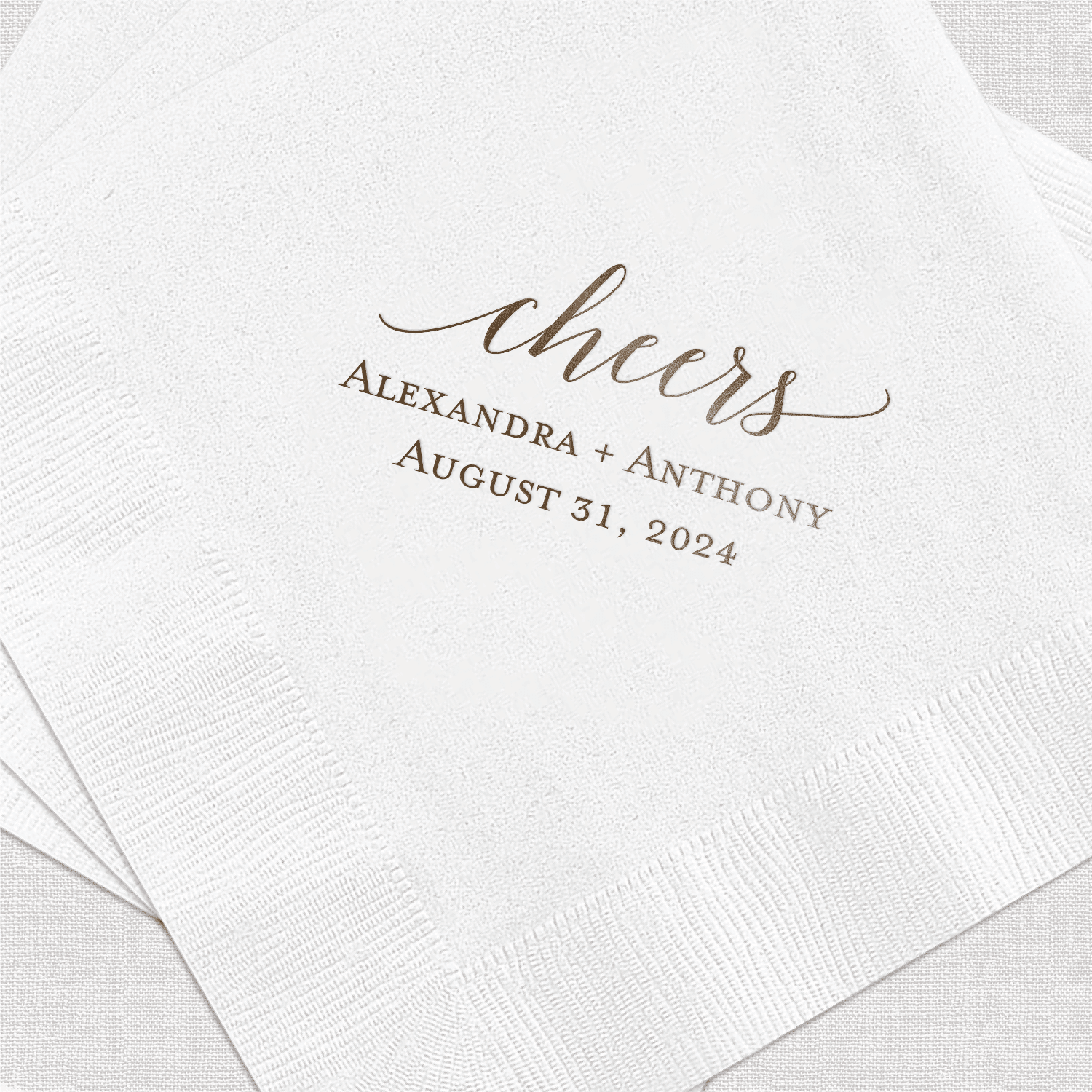 White napkin with gold foil stamped cheers design and personalized names Alexandra Anthony with wedding date August 31, 2024
