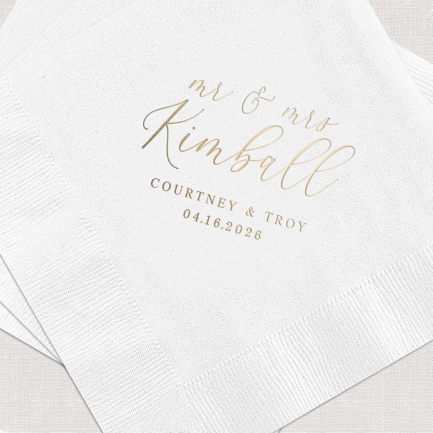 White napkin with gold foil stamped text reading "Mr and Mrs Kimball, Courtney Troy, 04.16.2026"