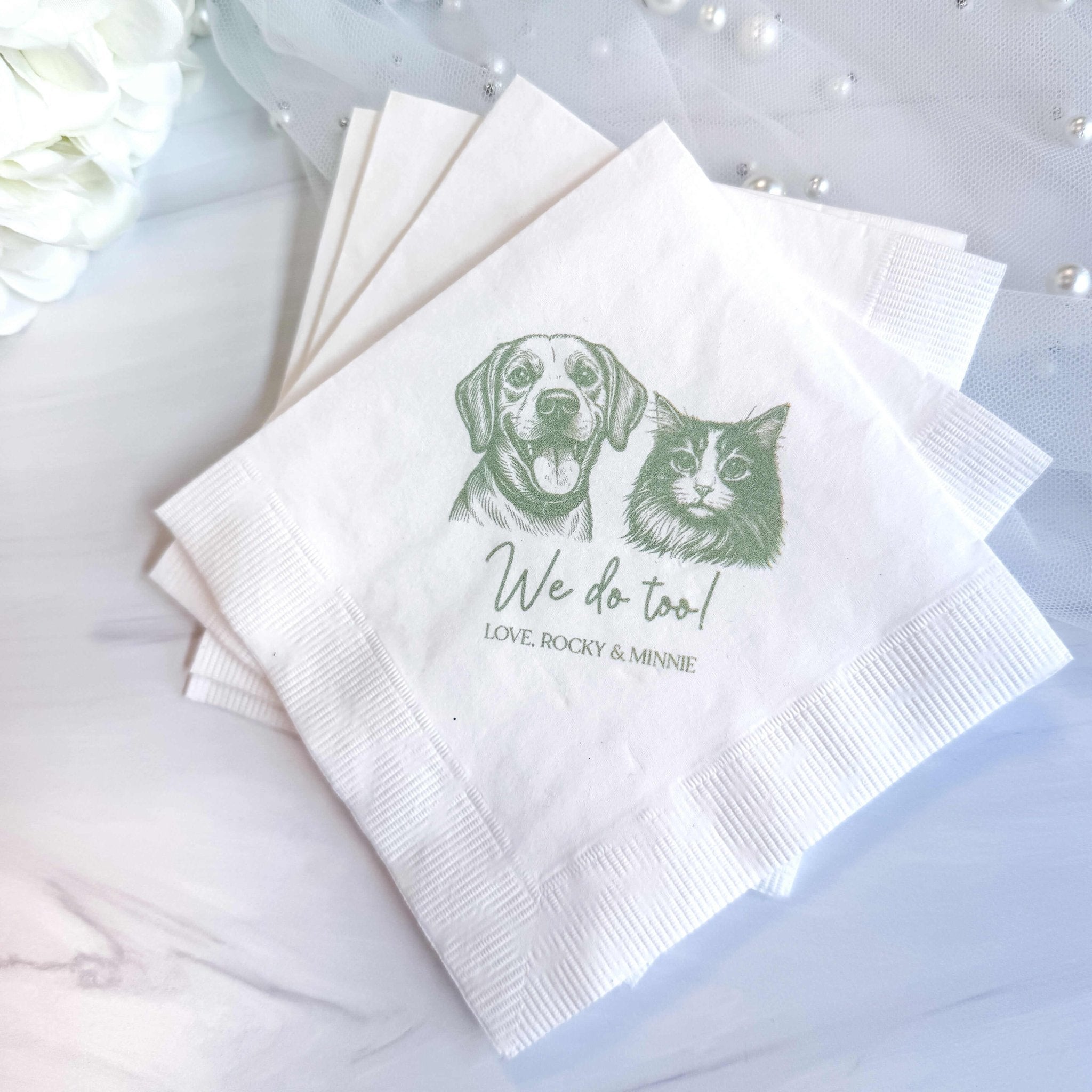 White napkins printed with dog and cat illustrations and "We do too!" personalization text for wedding favors.