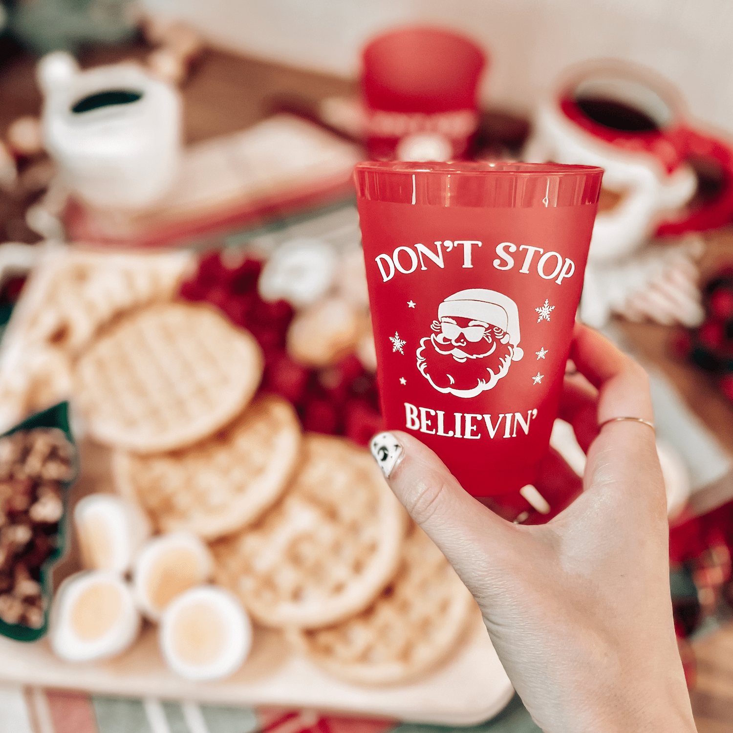 Red frosted cup with "Don't Stop Believin'" text and Santa graphic, held in hand at holiday party setting
