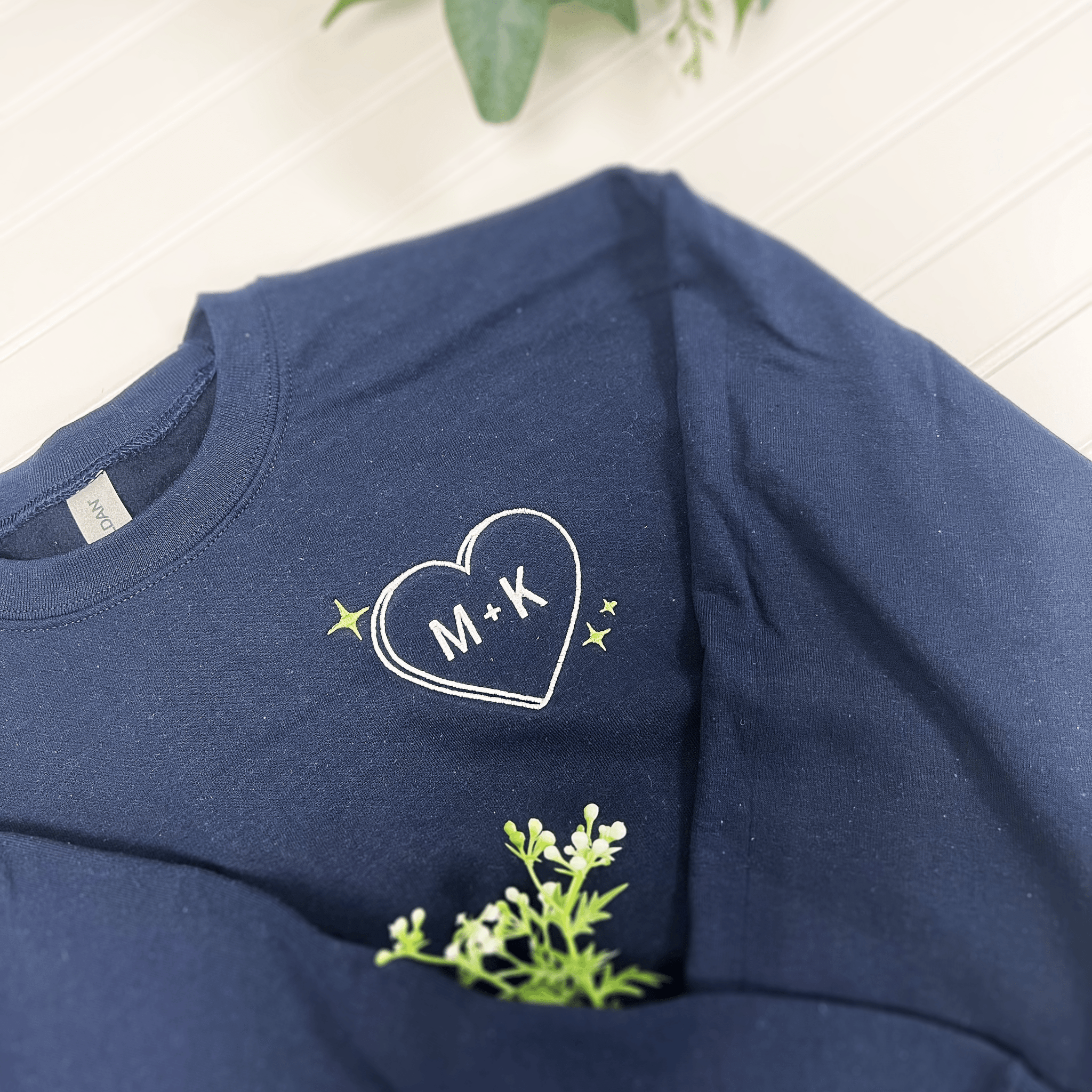 Navy sweatshirt with embroidered heart design containing initials M and K, surrounded by small stars