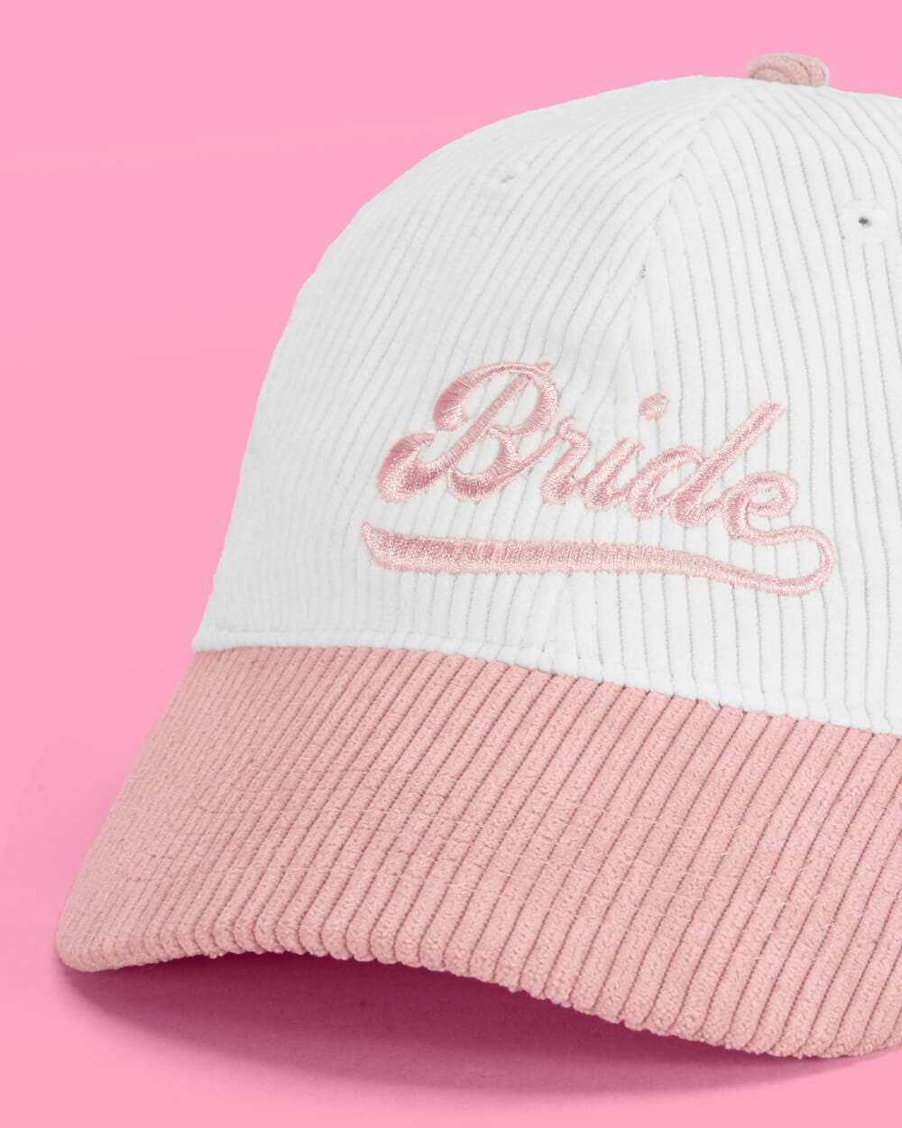 White and pink corduroy baseball cap with "Bride" embroidered in cursive script on front panel against pink background