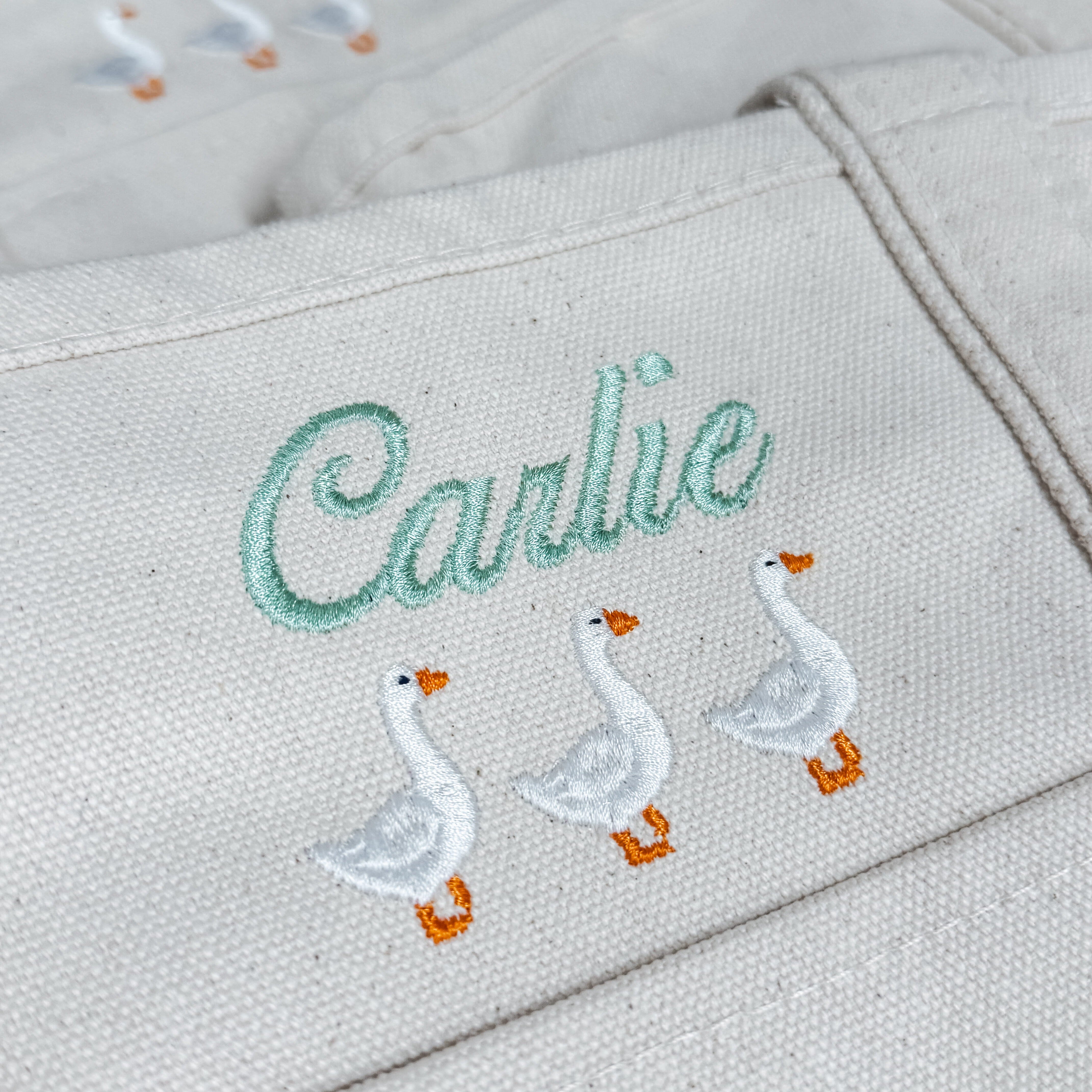 Close-up of personalized canvas tote embroidered with the name Carlie and three white geese