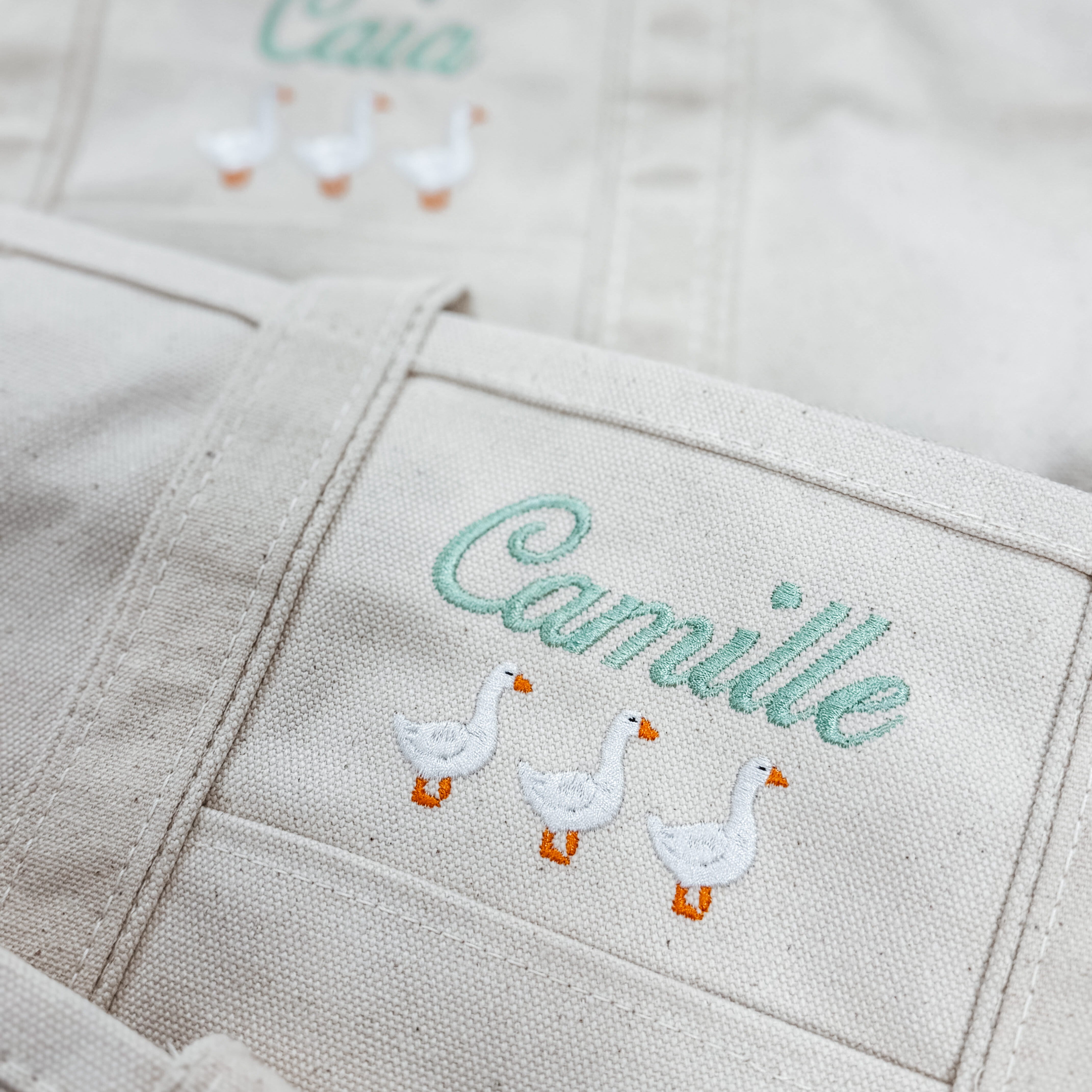 Personalized canvas goose tote embroidered with the name Camille above three white geese