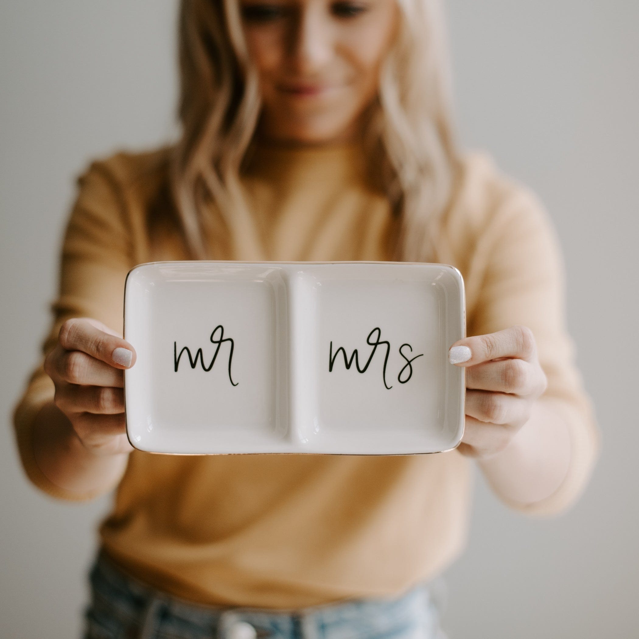 White ceramic two-section dish with "mr" and "mrs" handwritten text, held by woman in tan sweater.