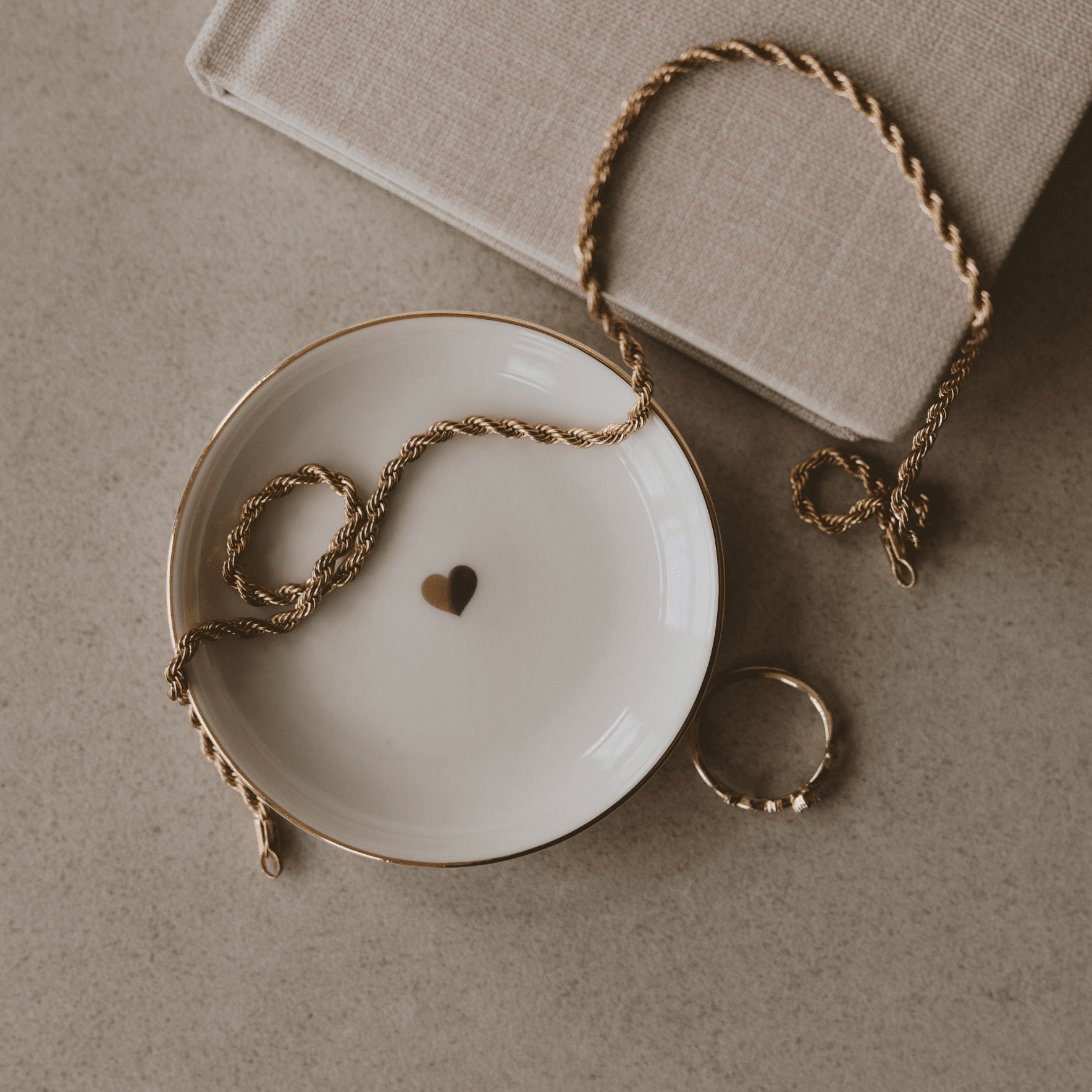 White ceramic dish with gold rim, small heart detail, and twine handle for hanging, displayed with matching ring holder.