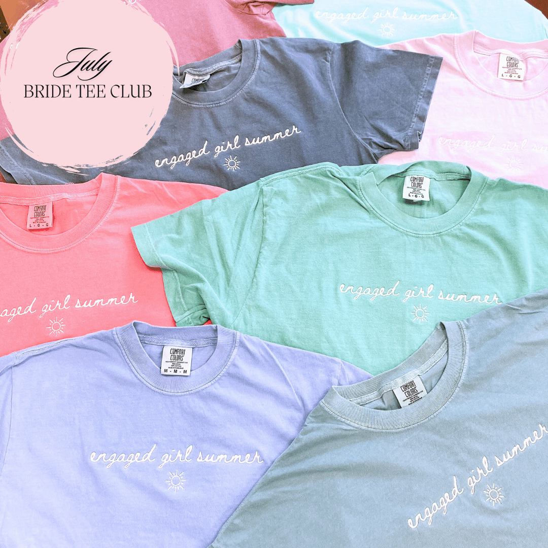 Colorful stack of t-shirts in pink, mint green, lavender, and gray with "engaged girl summer" text printed across chest, featuring Rubi & Lib Bride Tee Club logo.