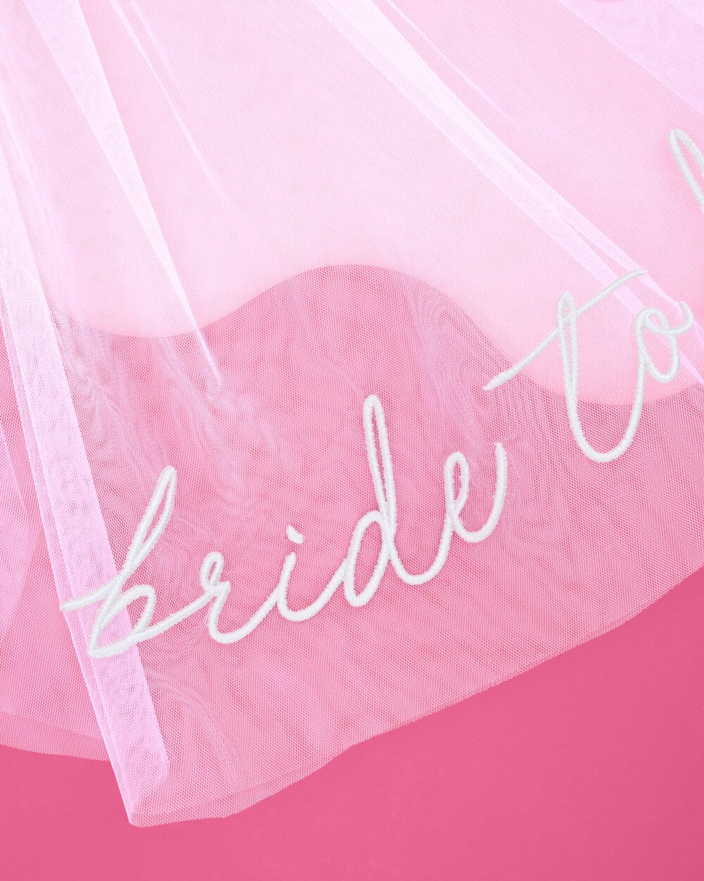 White embroidered veil with "Bride To Be" script text on sheer pink tulle fabric.